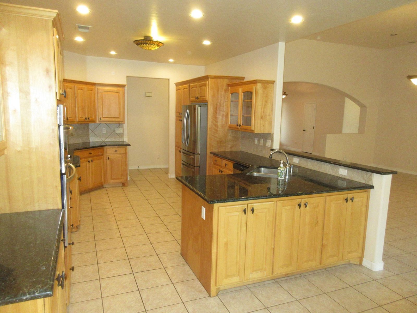 Kitchen with light wood cabinets, dark countertops, tile floor, and an island.