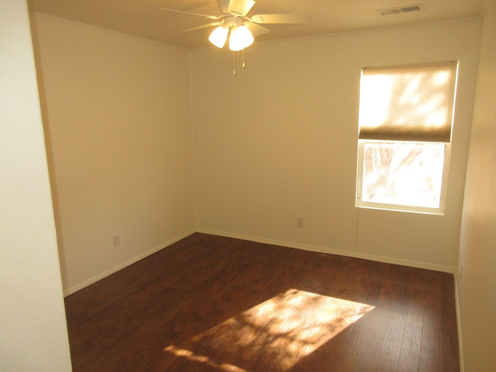 Empty room with wood-look floor, window with shade, ceiling fan, and off-white walls.