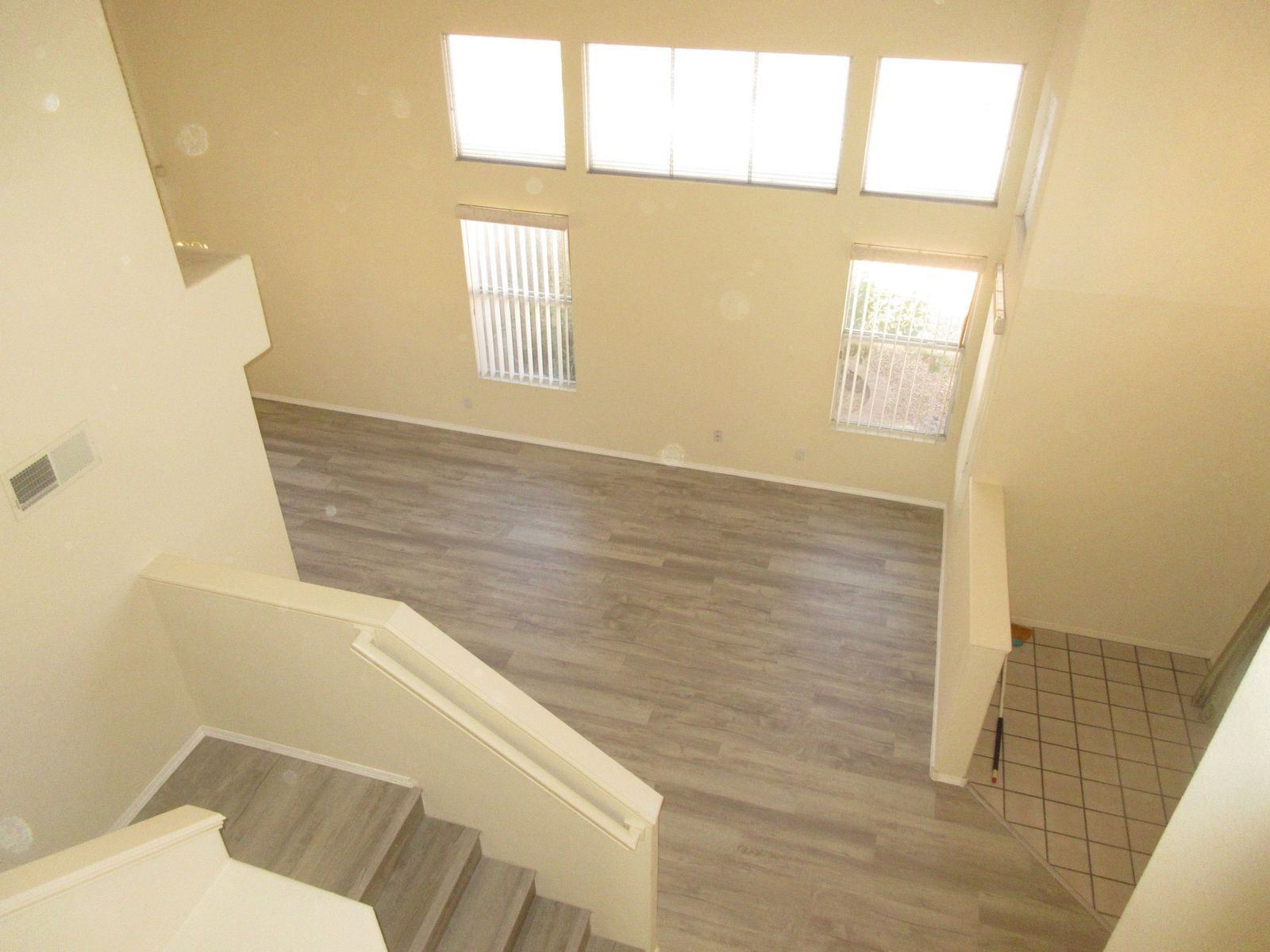 View from a staircase down into a room with large windows, light wood-look flooring, and neutral walls.