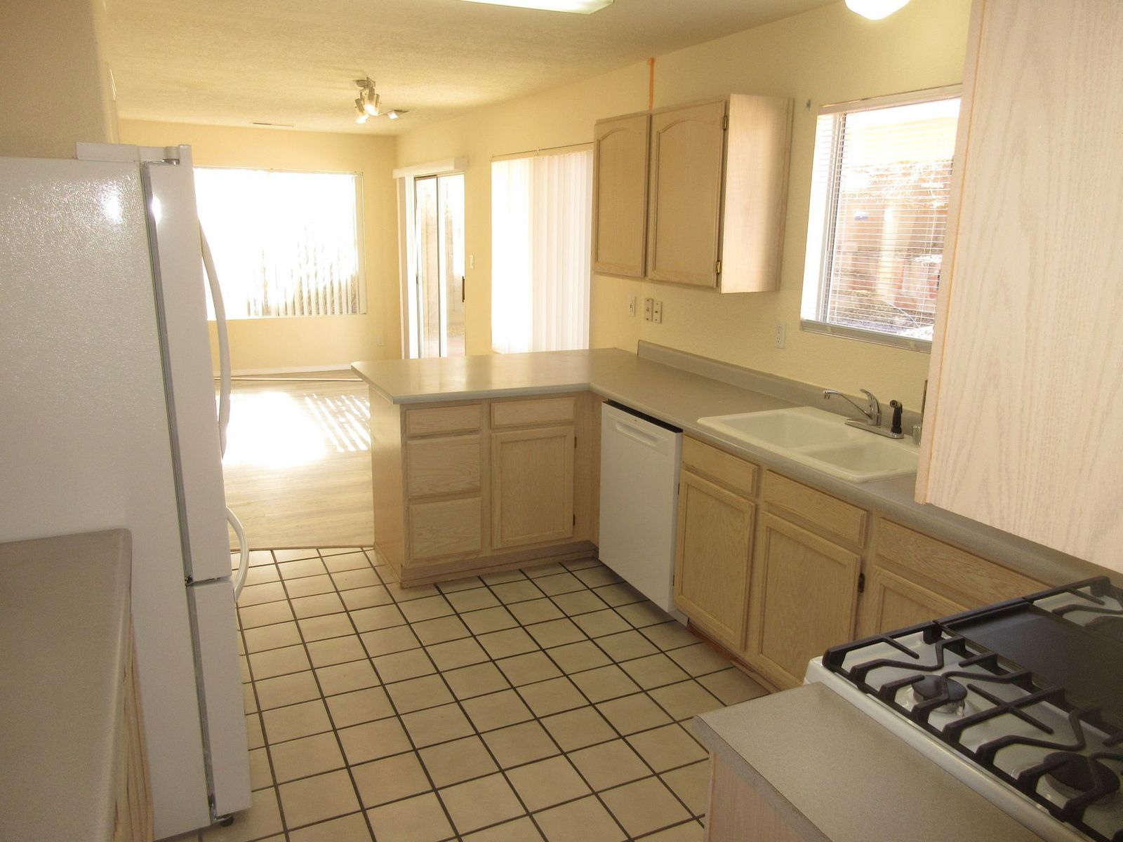 Kitchen with light cabinets, white appliances, tile floor, and view into the living room.