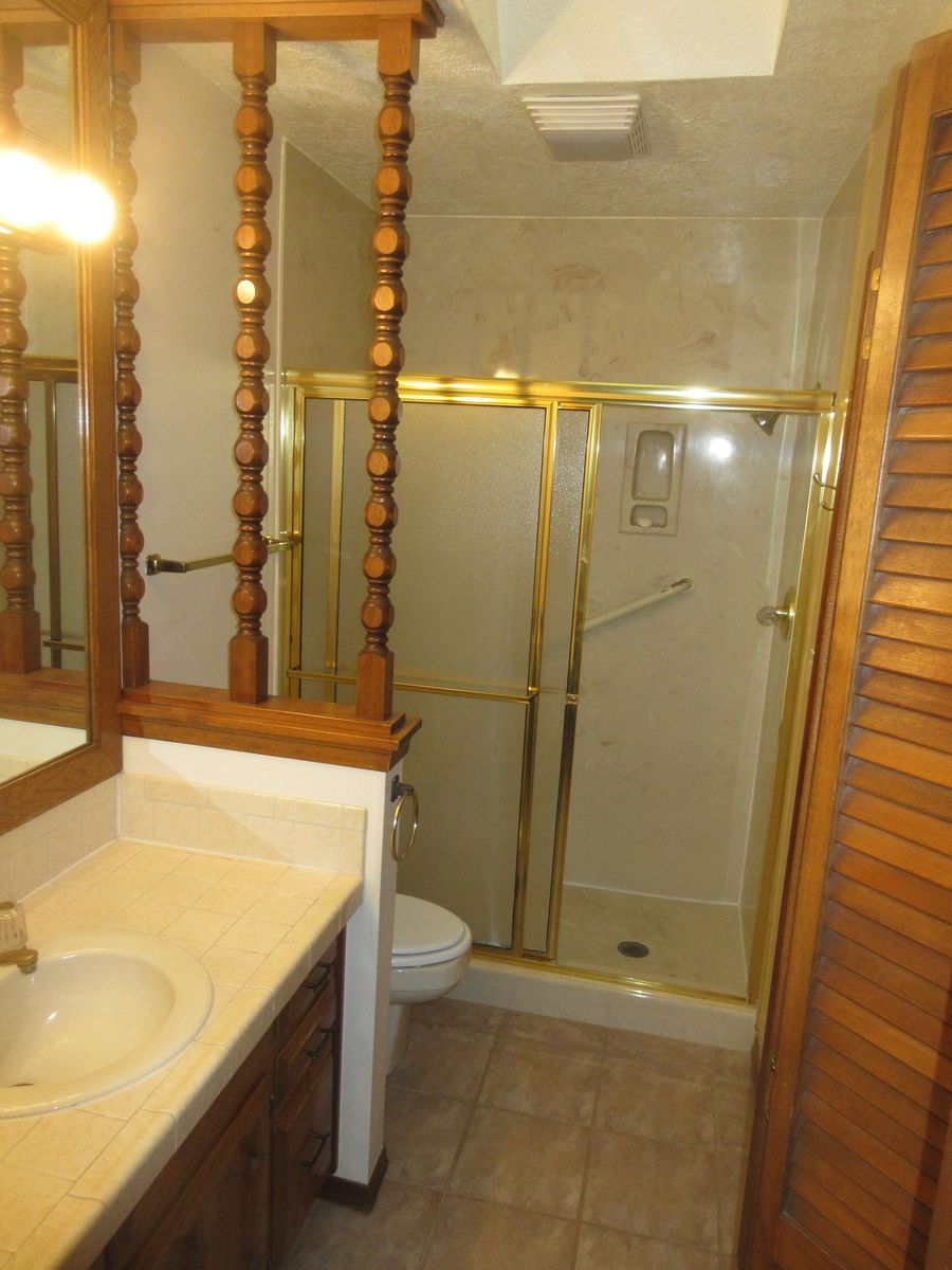 Bathroom with a sink, toilet, and shower with gold trim, brown wood accents and a closed wooden door.