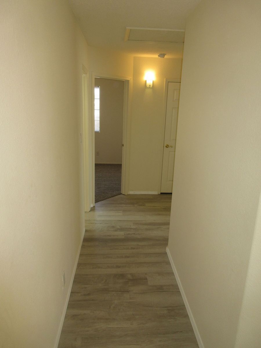 Narrow hallway with beige walls and light wood-look flooring. Doors lead to other rooms.