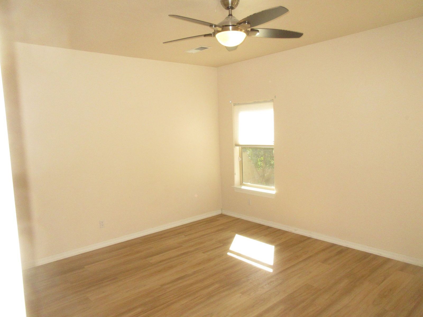 Empty room with light wood floors, a window, and a ceiling fan.