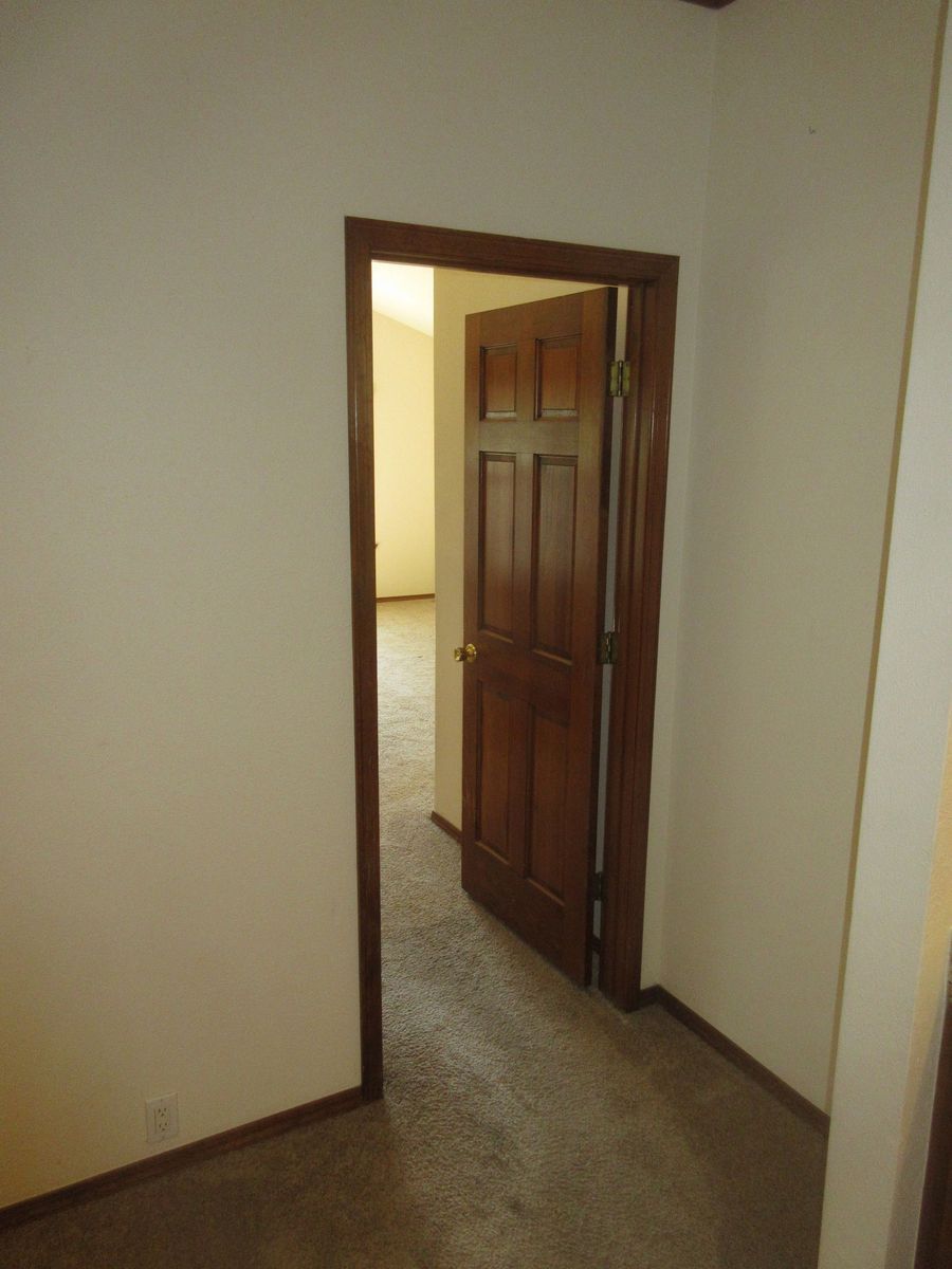 Open doorway with wooden door and frame, beige walls, and carpet.