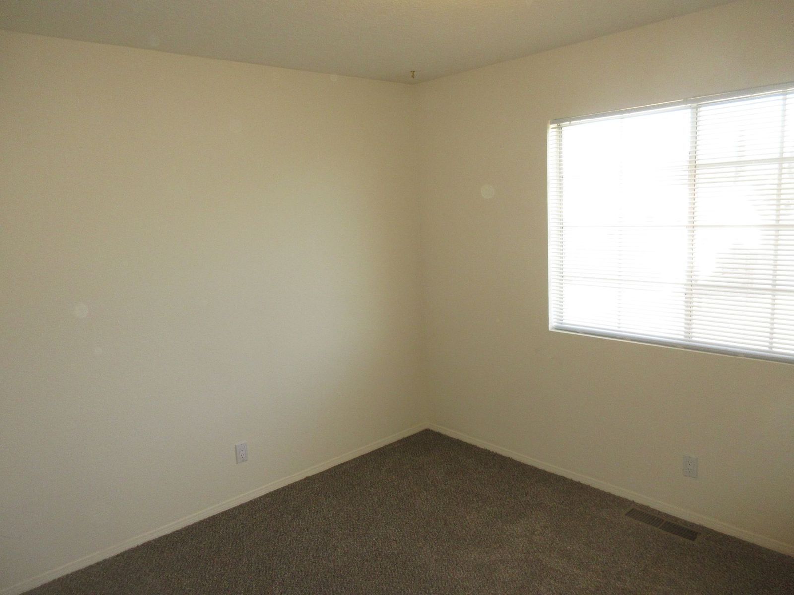 Empty room with beige walls, brown carpet, and a window with blinds.