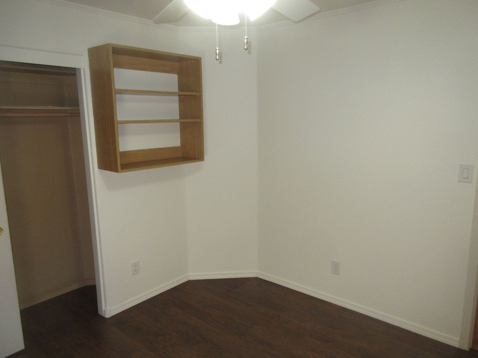 Empty room with dark wood floor, white walls, closet, and wall-mounted bookshelf.