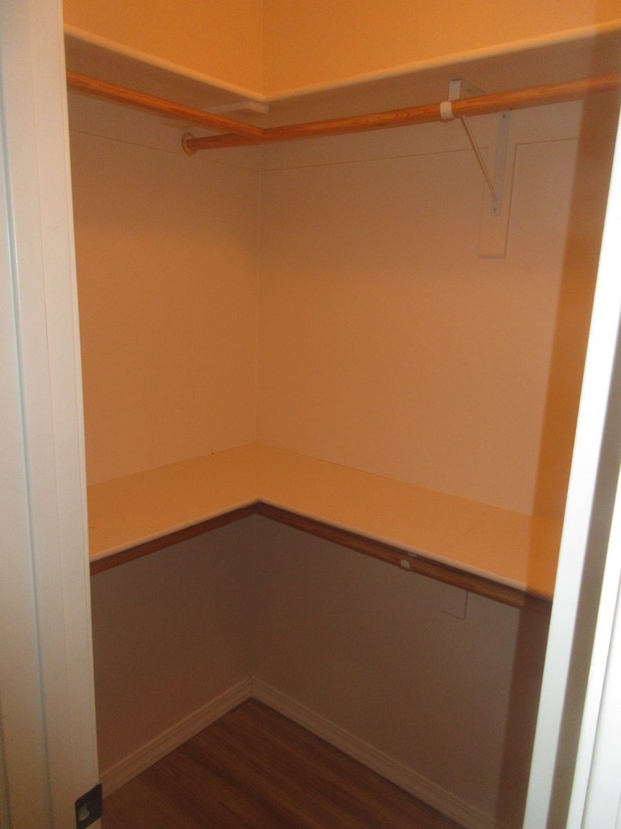 Empty closet with shelf and clothes rod; wooden floor, tan walls.