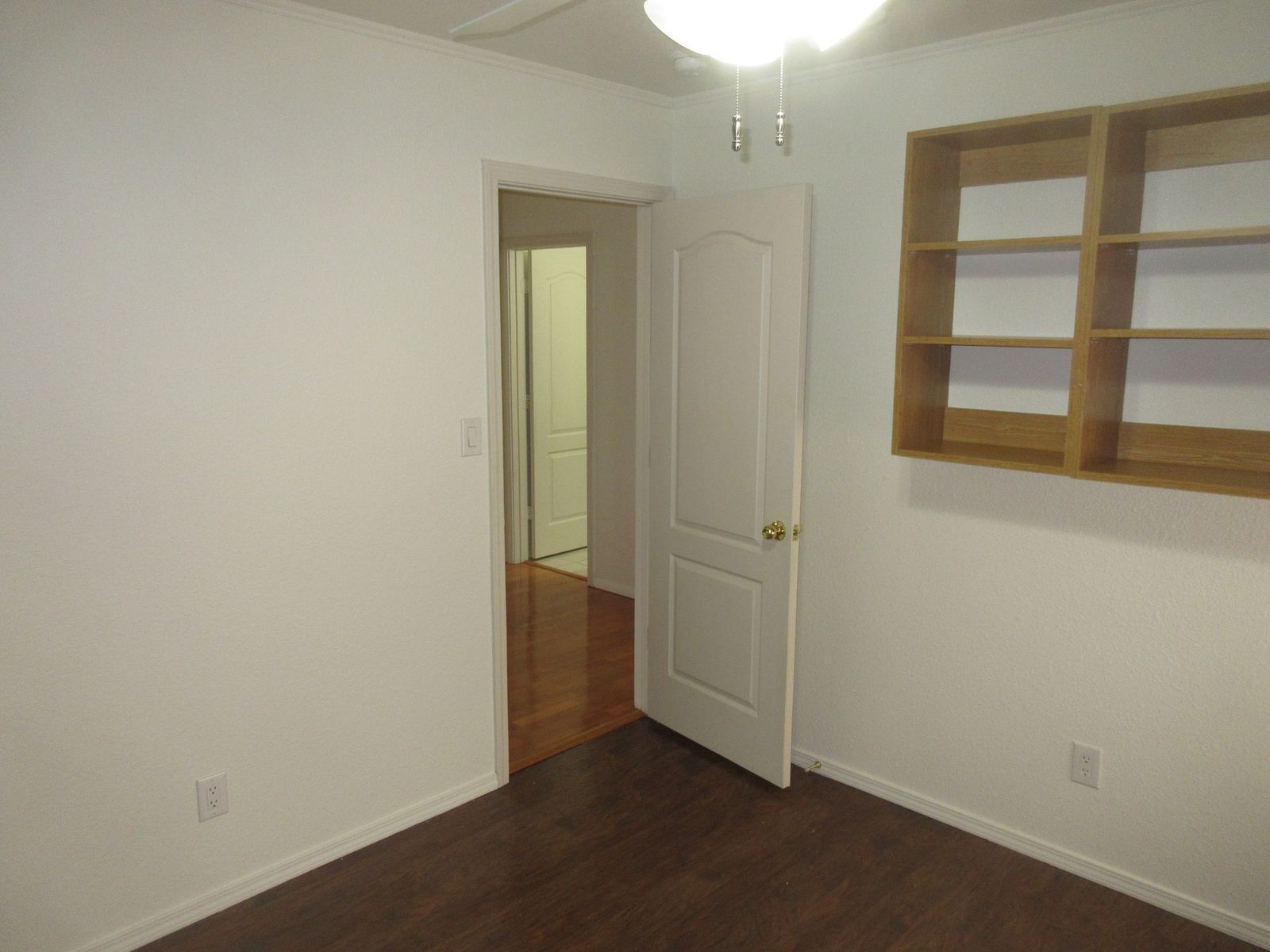Empty room with white walls, a closed white door, and a built-in wooden shelf.