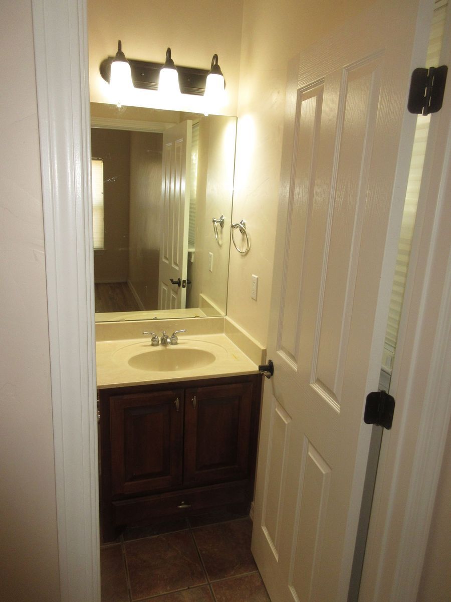Bathroom with vanity, mirror, and open door. Brown cabinet, white sink, and light fixture.