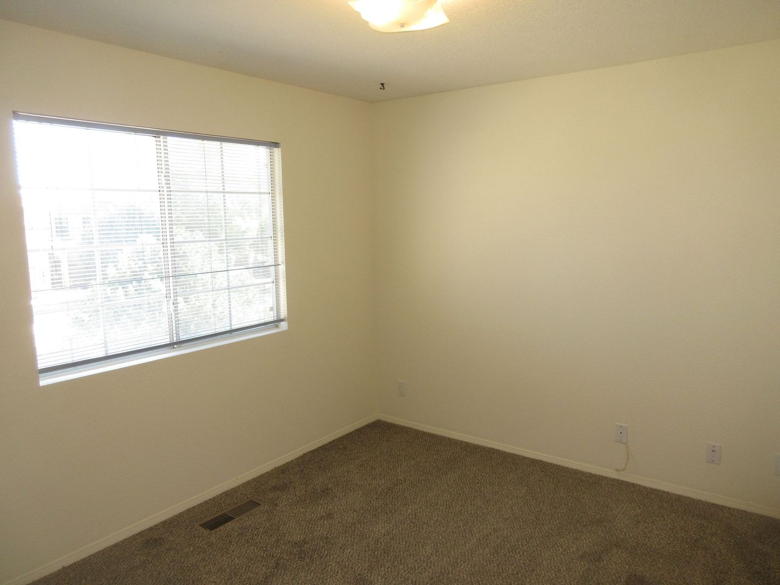 Empty room with beige walls, brown carpet, and a window with blinds.