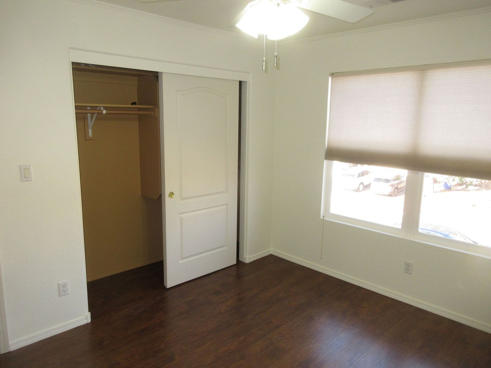 Empty bedroom with closet, wood floor, window with blinds.