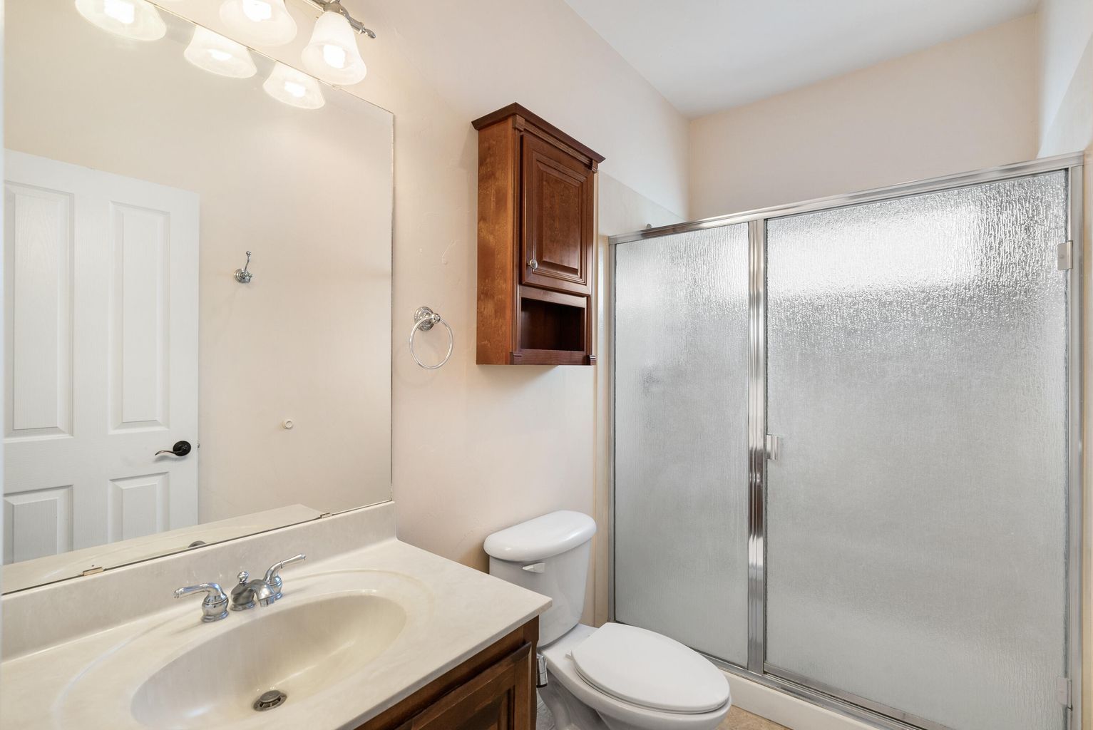 Bathroom with white walls, vanity, toilet, shower with frosted glass doors, and a small wooden cabinet.