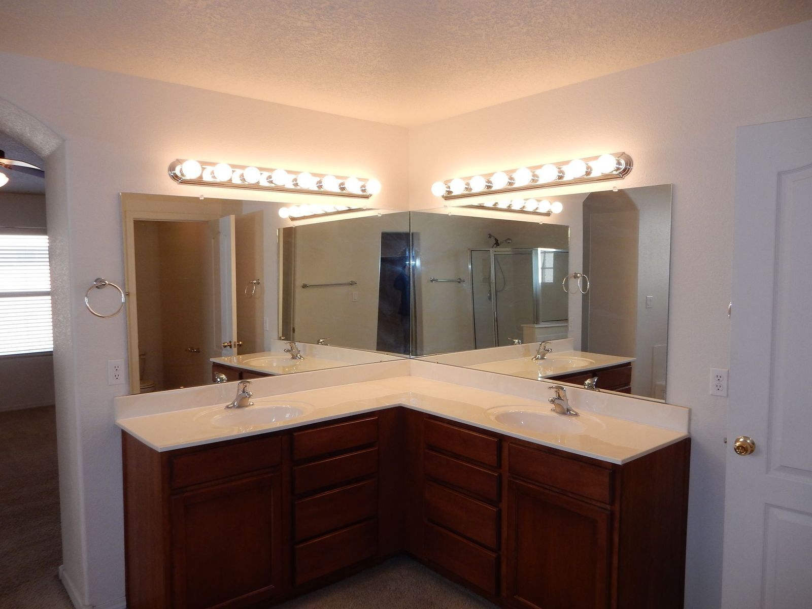 Bathroom with corner vanity, two sinks, large mirrors, and overhead lighting. Dark brown cabinets, white countertop.