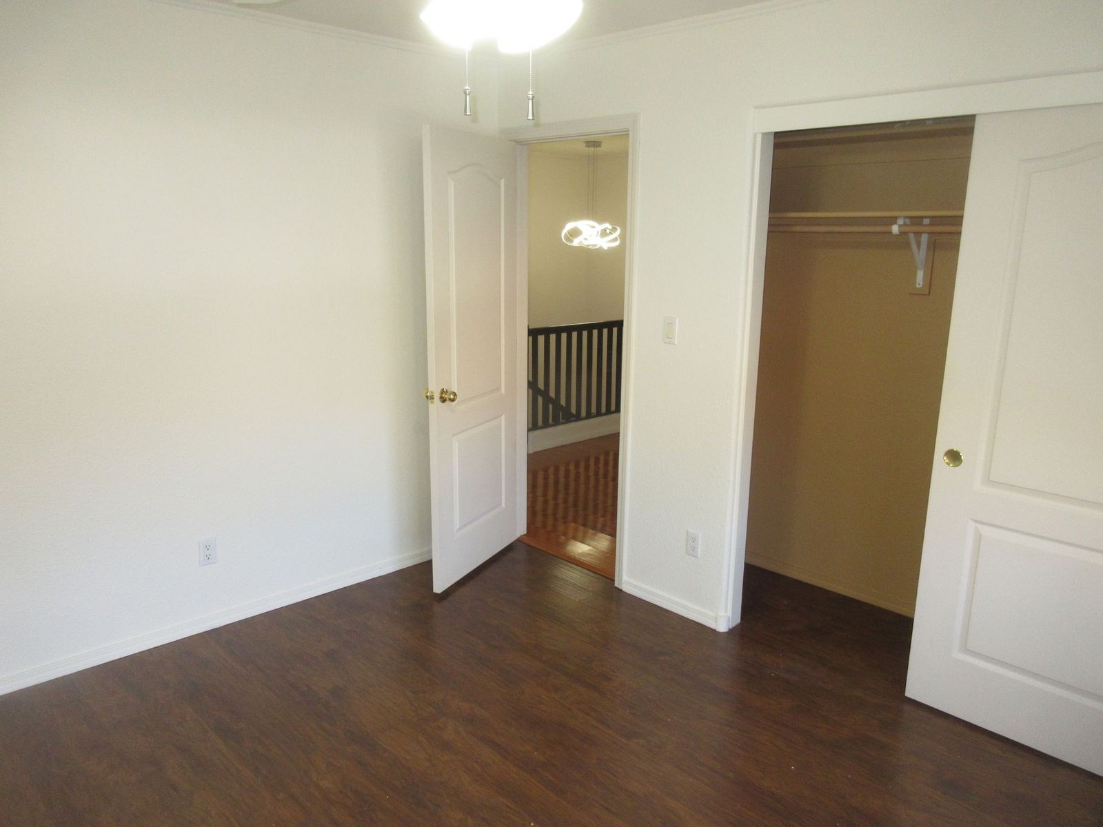 Empty room with hardwood floors, a closet, and a doorway leading to stairs.