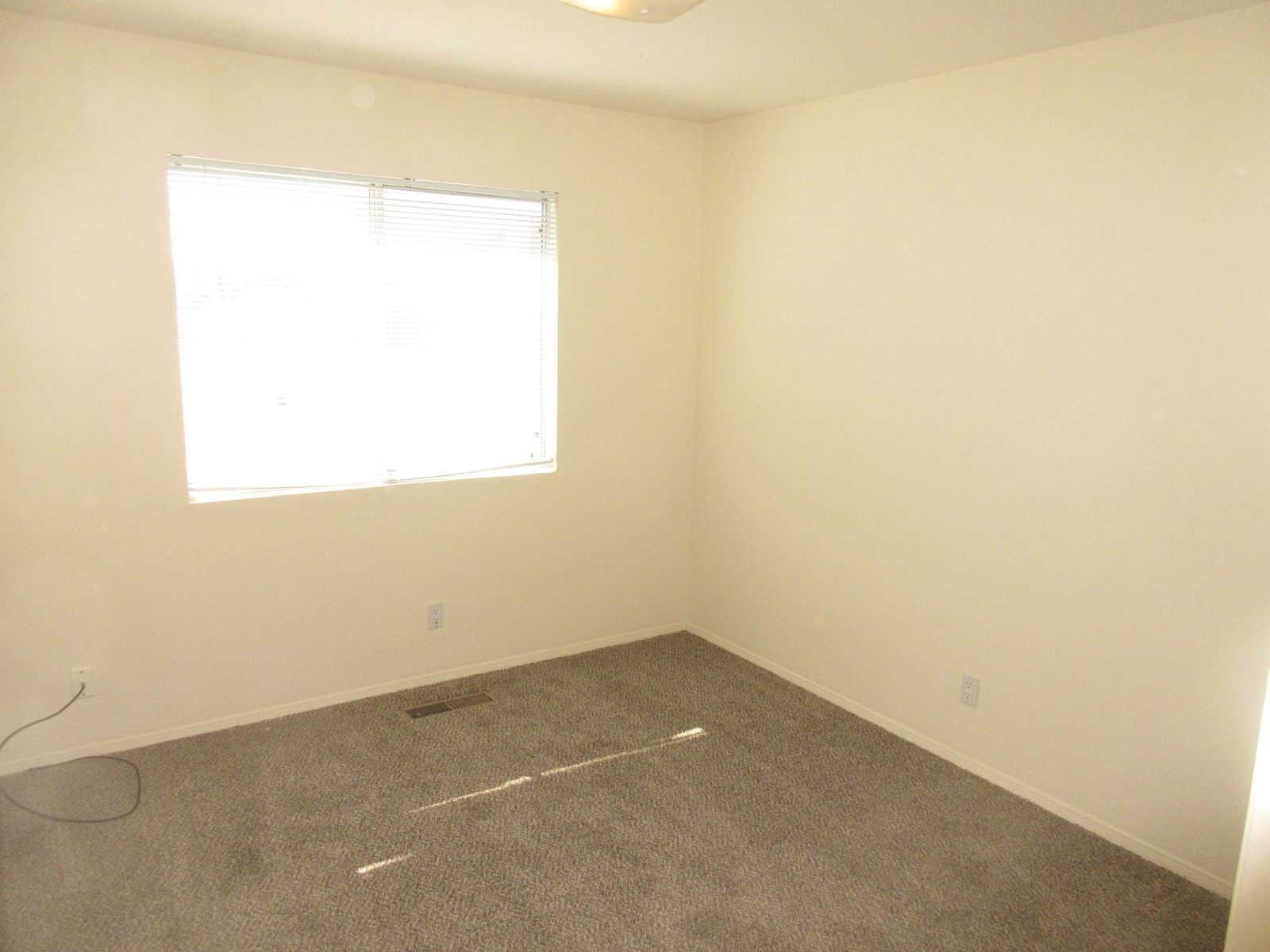 Empty room with tan walls, a window with blinds, and gray carpet.