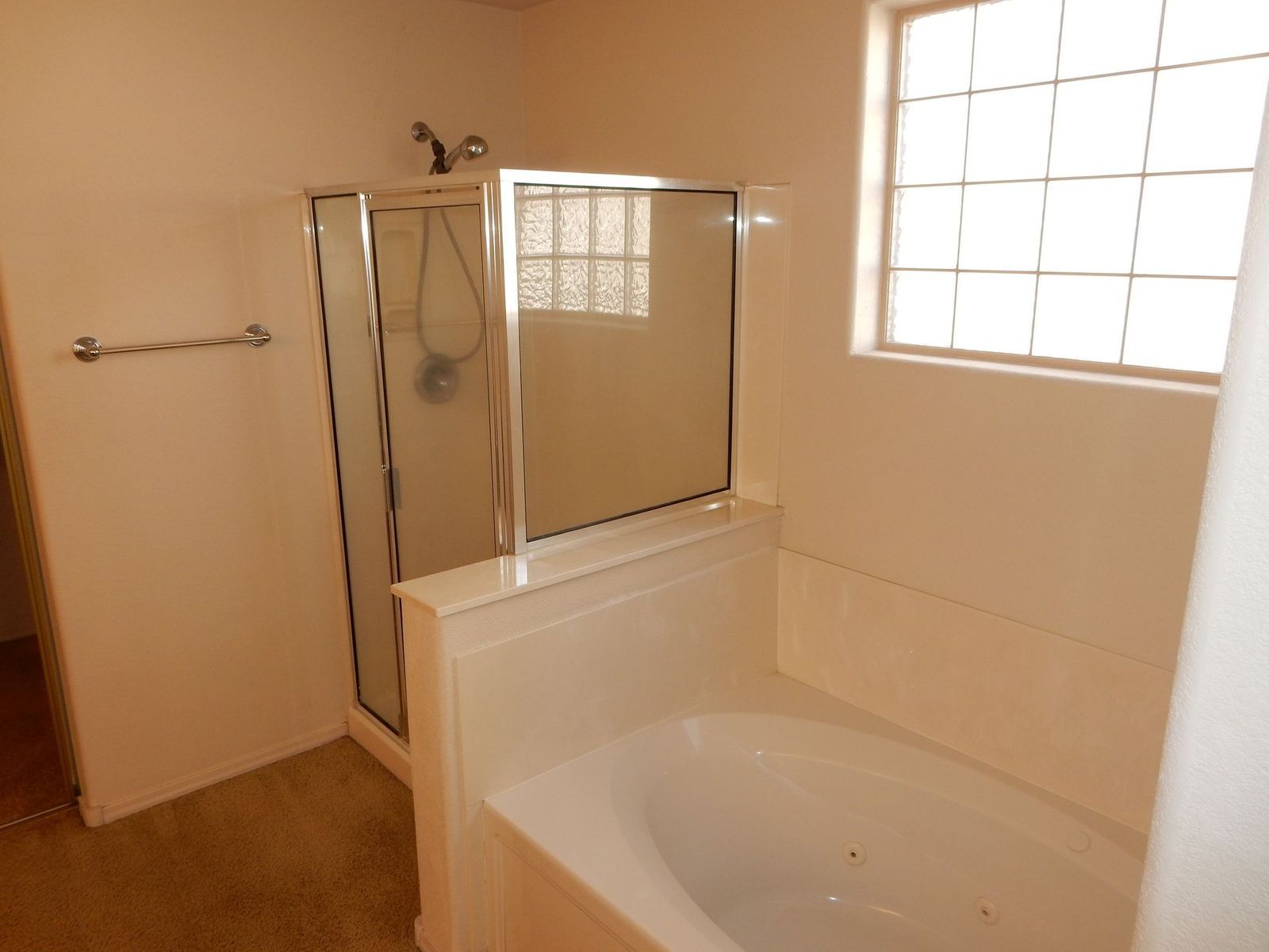 Bathroom with a shower and bathtub. Light beige walls, a window, and a white tub.