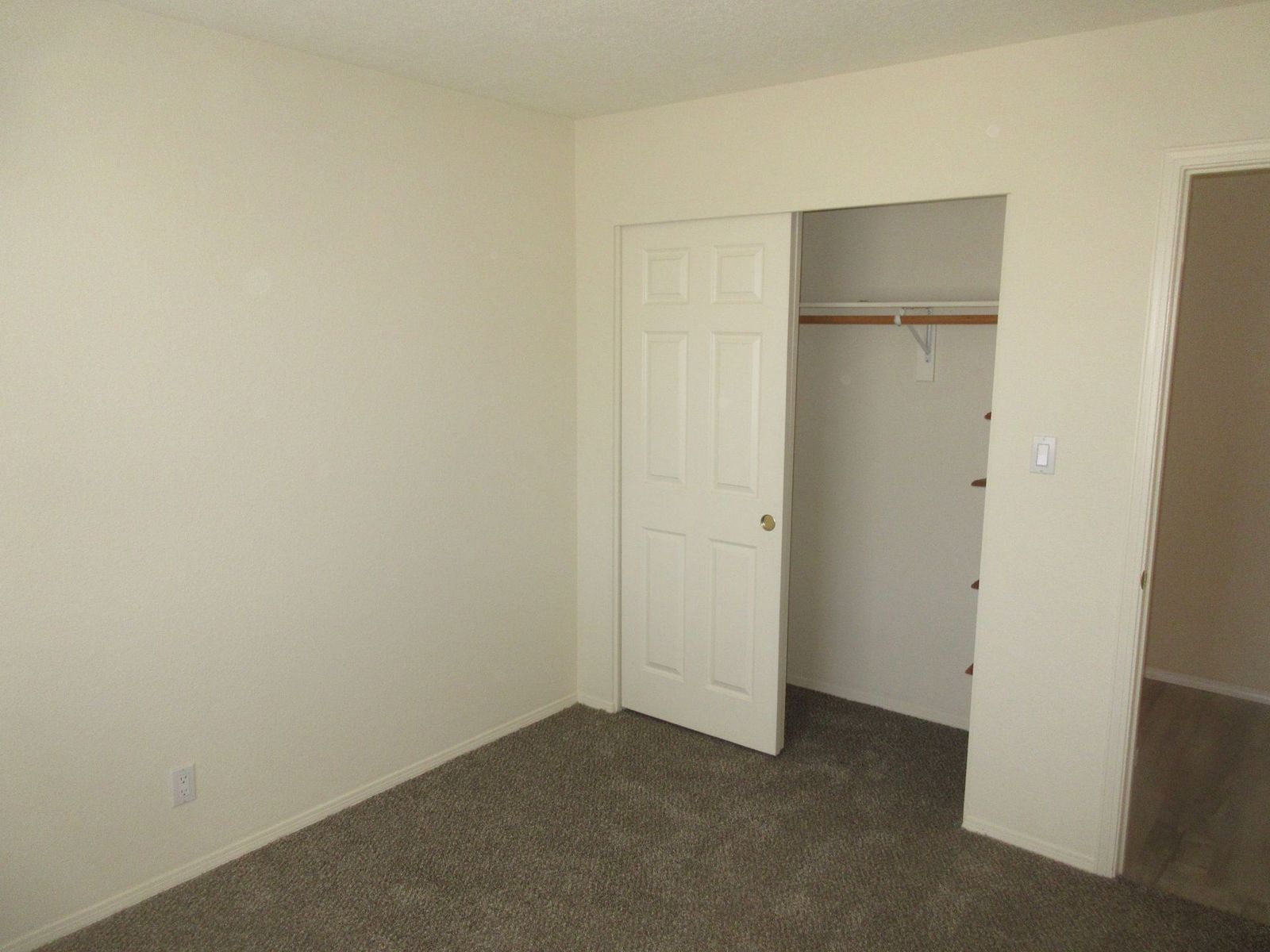 Empty bedroom with tan walls, brown carpet, and a partially open closet.