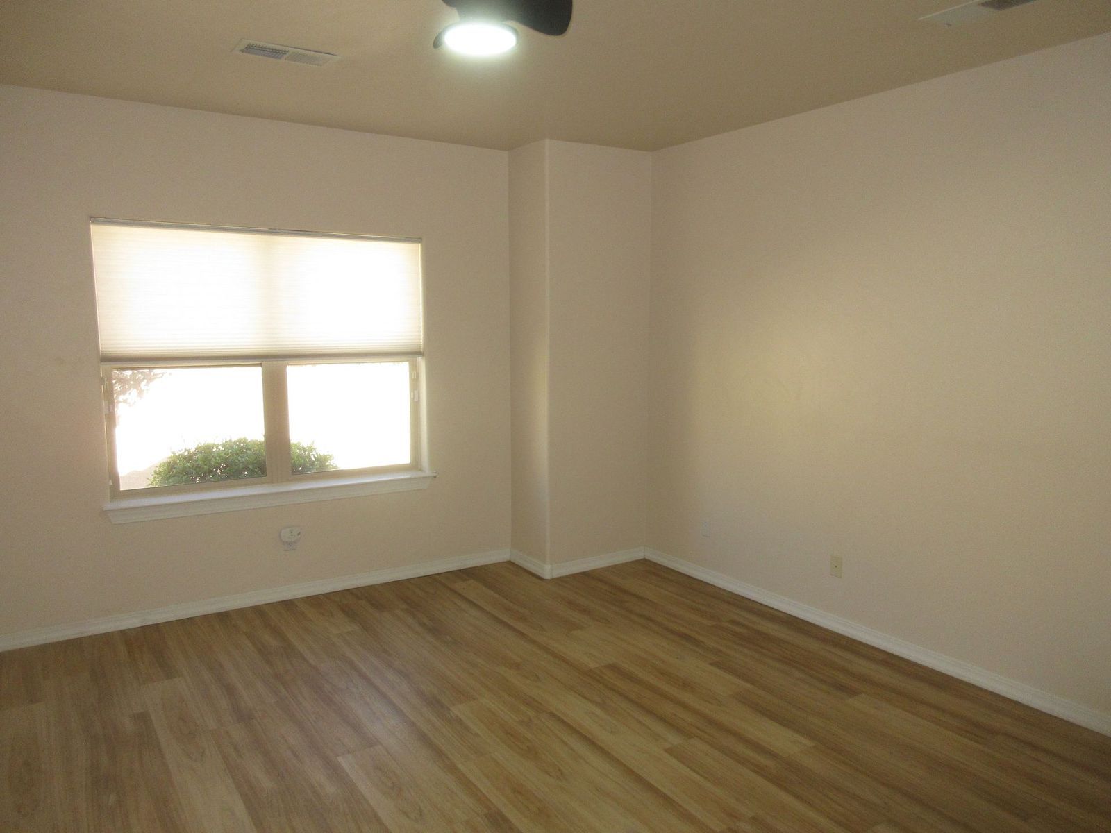 Empty room with light wood flooring, a window with shades, and beige walls.