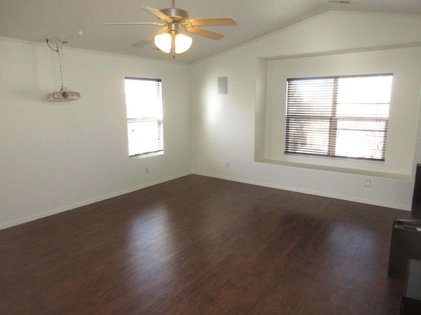 Empty room with wood-like floors, two windows with blinds, a ceiling fan, and a projector.