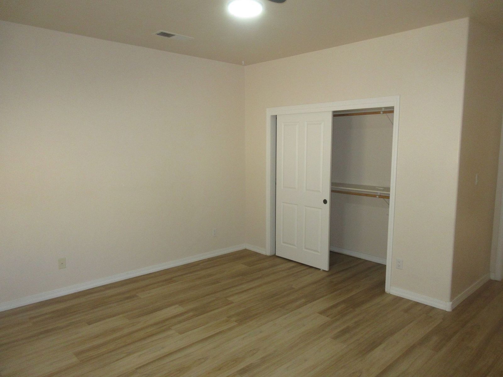 Empty room with light wood floor, beige walls, and closet.