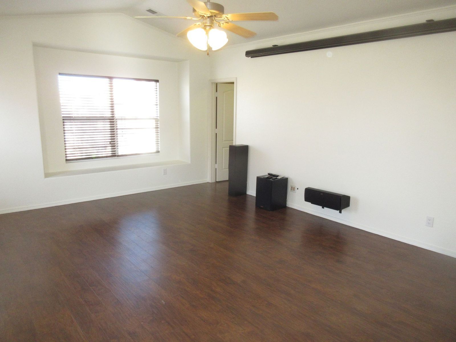 Empty living room with wood flooring, white walls, and a window with blinds.