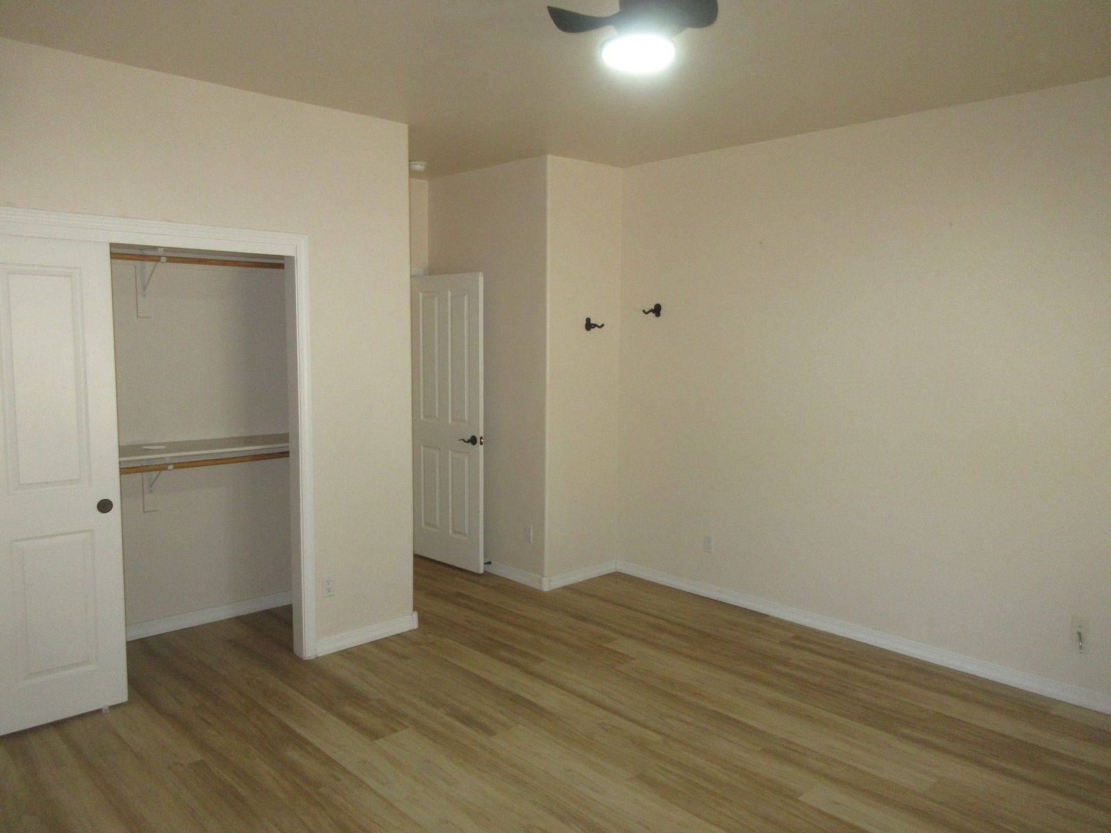 Empty bedroom with hardwood floors, closet, and a white door leading to another room.