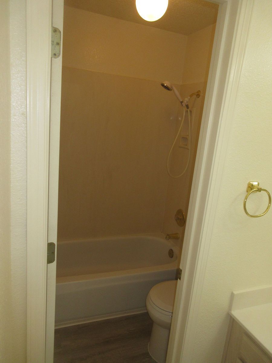 Bathroom doorway view; tub, toilet, and showerhead visible. White walls, beige tub surround.