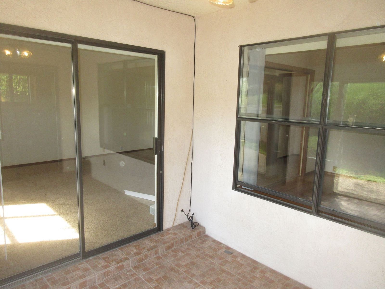 Patio with sliding glass door and windows reflecting interior rooms and natural light. Brown tile floor.