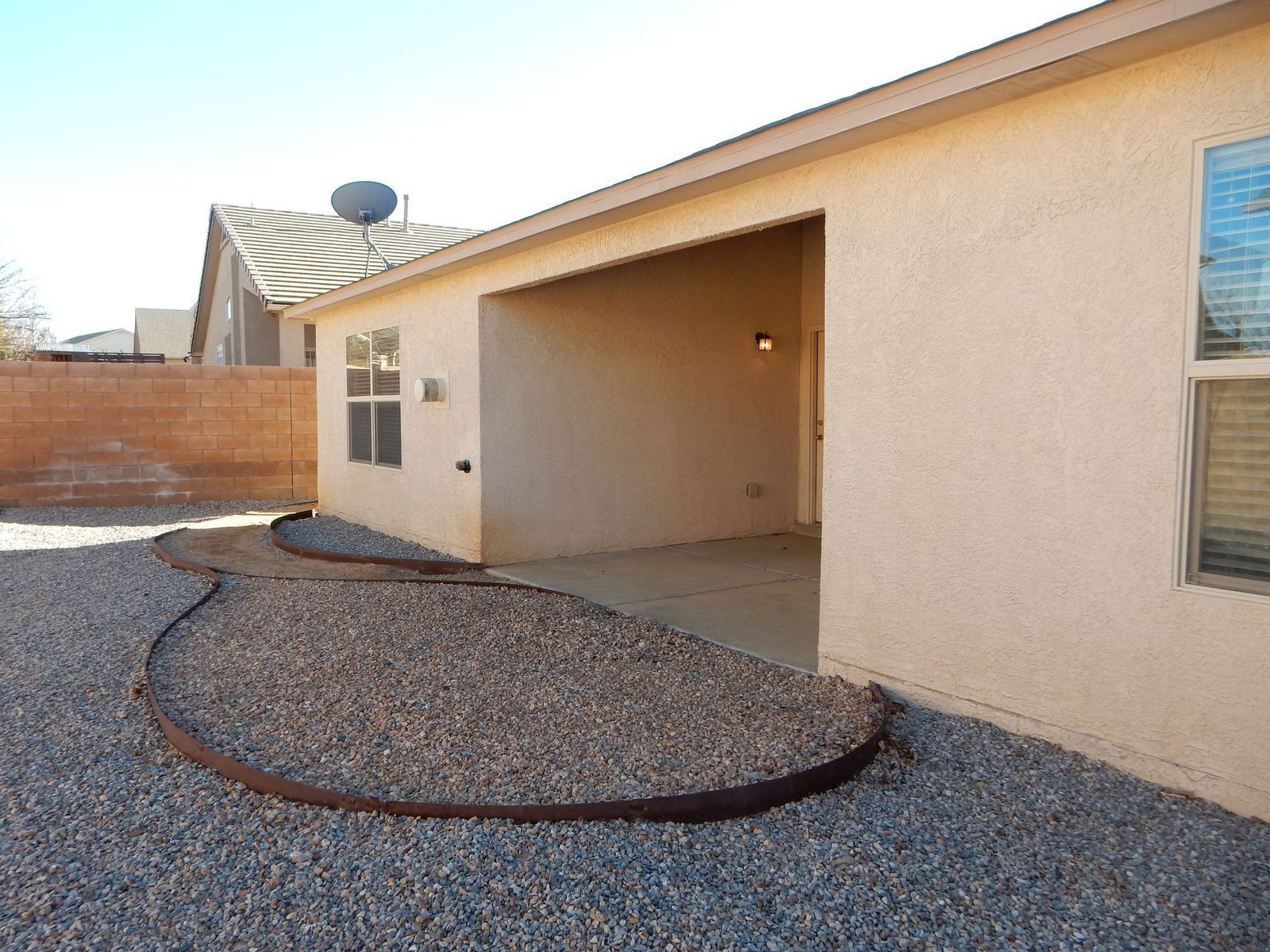 Backyard with gravel ground, covered patio, and house in the background.