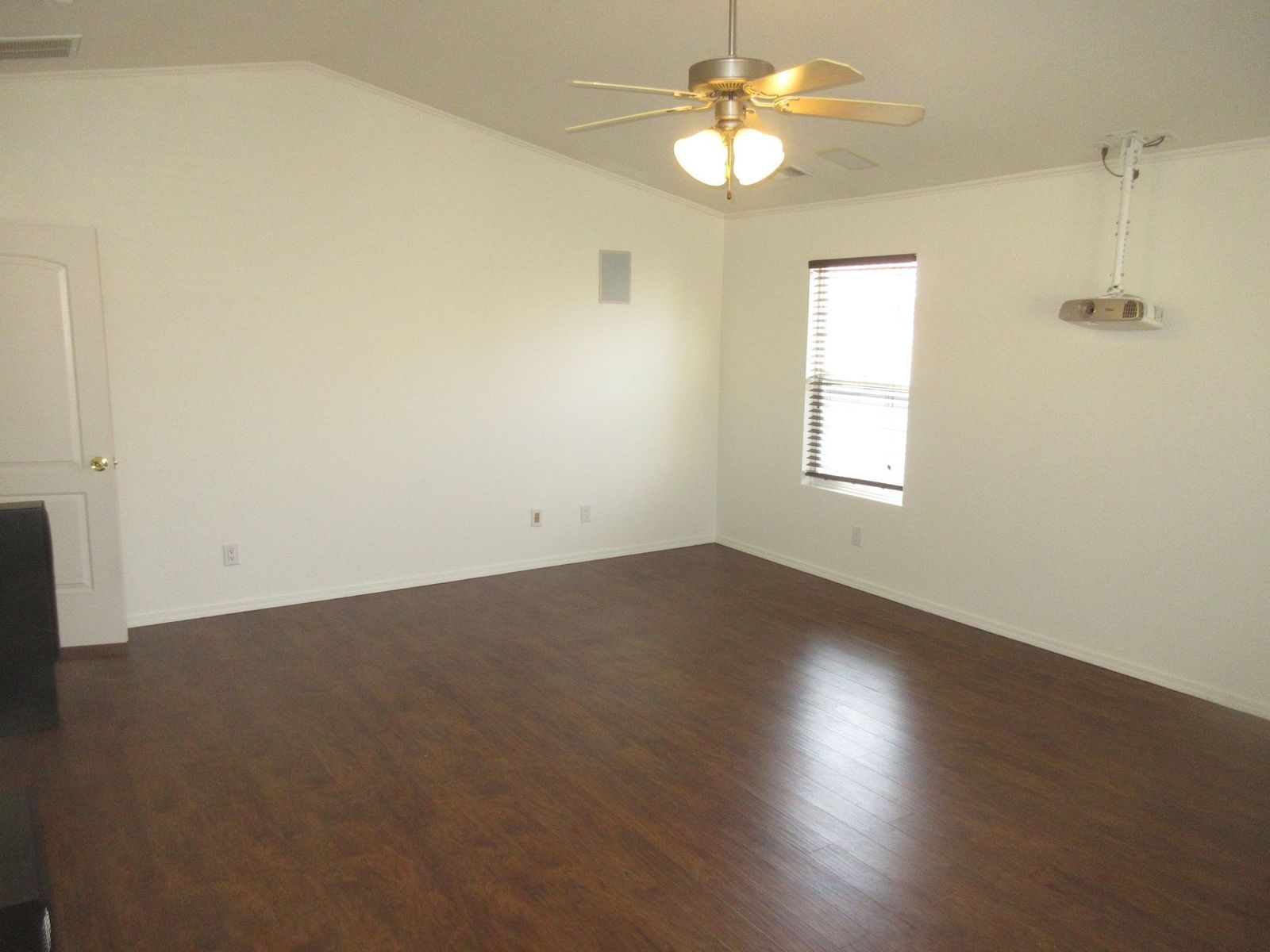 Empty room with wooden floor, white walls, ceiling fan, and a window.