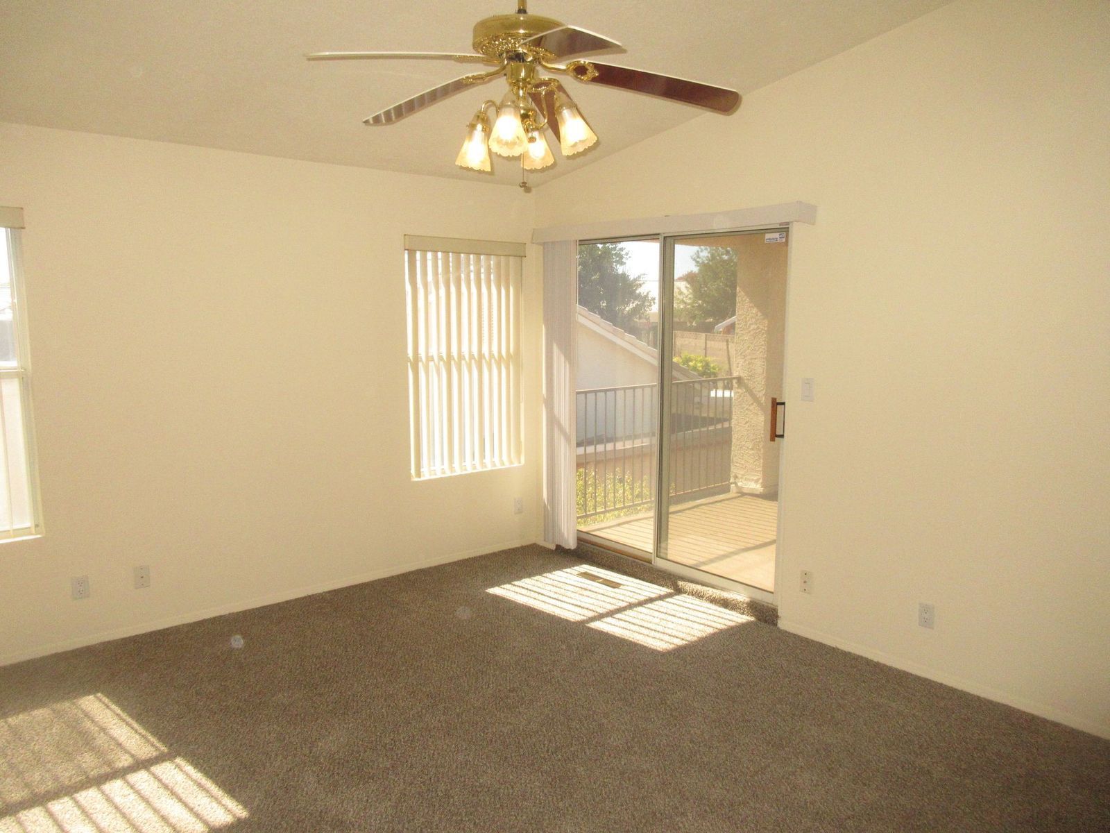 Empty room with beige walls, brown carpet, ceiling fan, sliding glass door to a patio, and a window with blinds.