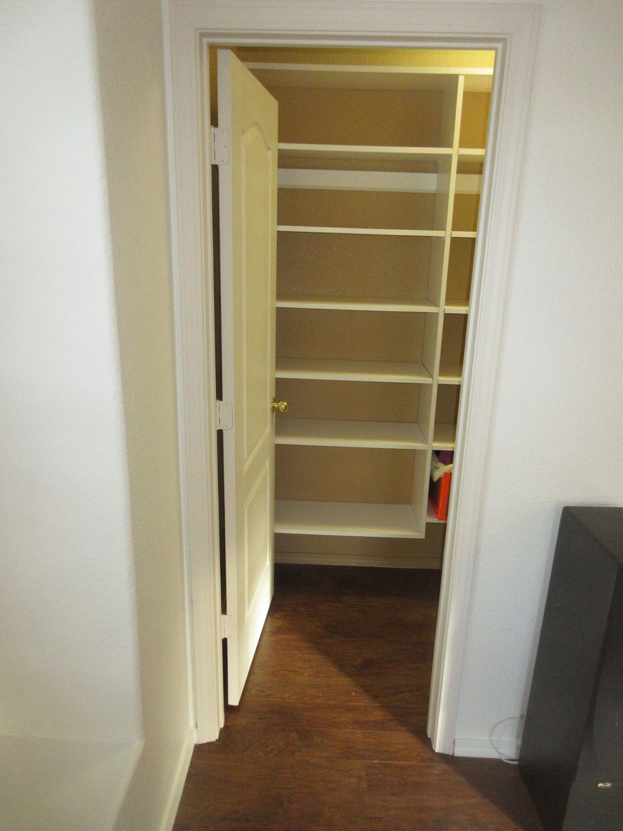 White door opens to reveal a closet with white shelves. Dark wood floor.