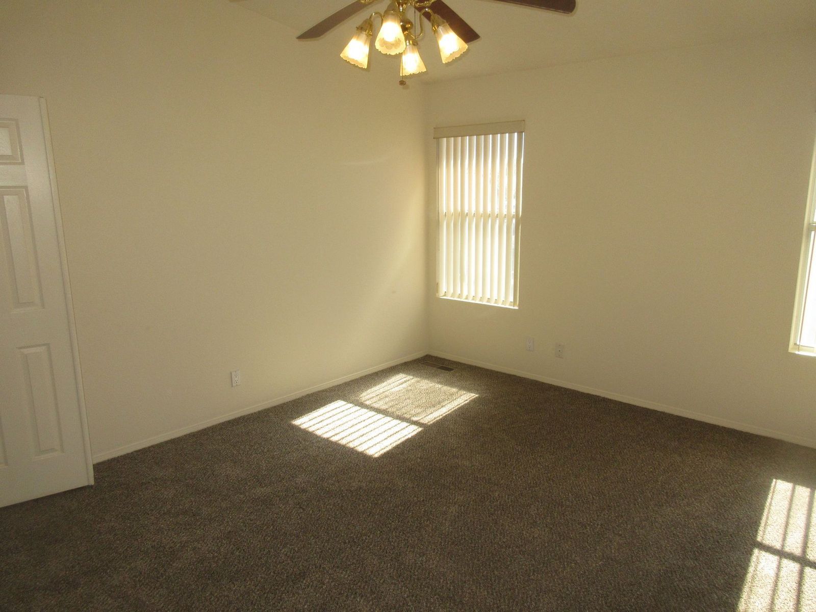 Empty bedroom with neutral walls, dark carpet, and a window with blinds.