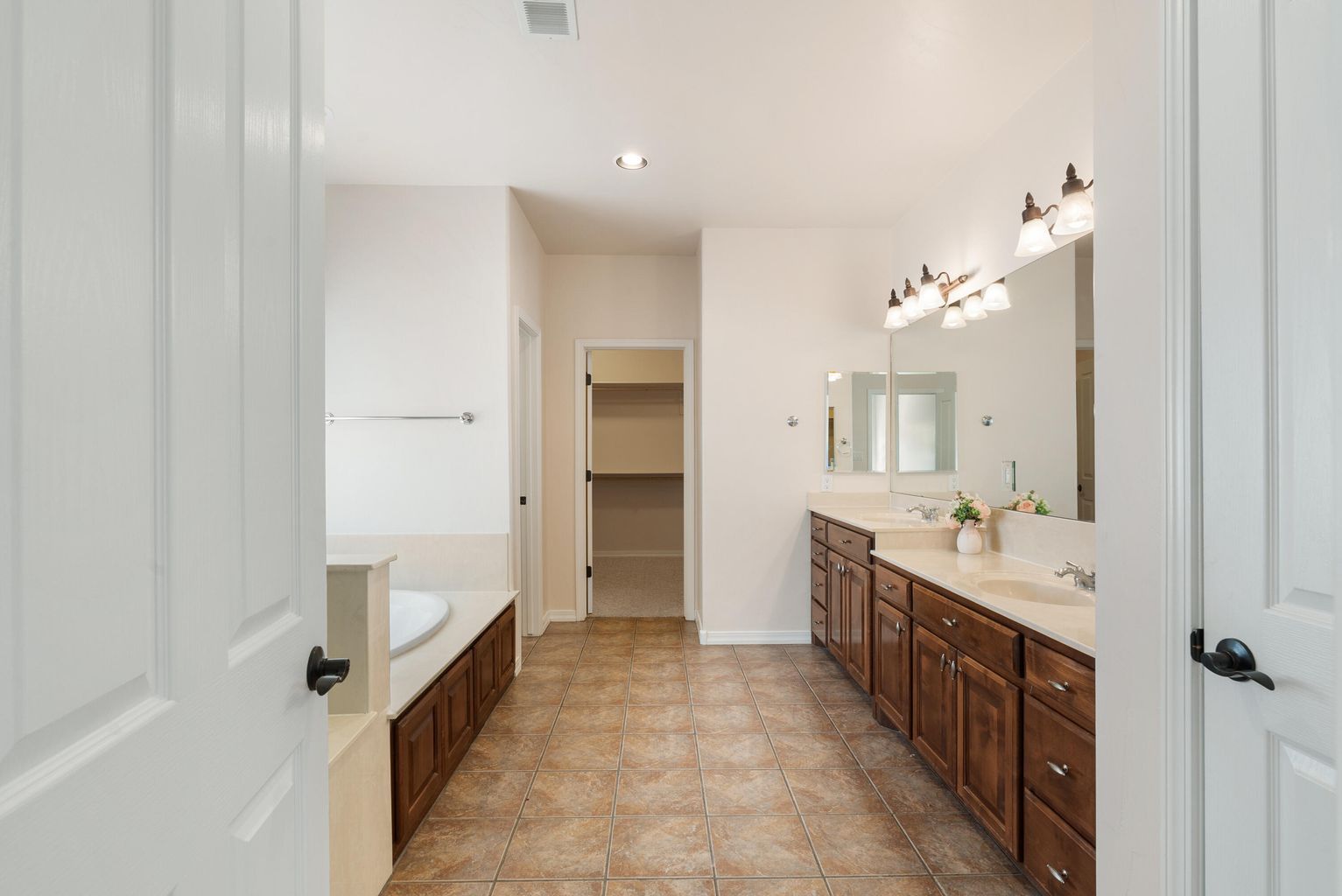 Bathroom with brown cabinets, tile floor, walk-in closet, and a tub.