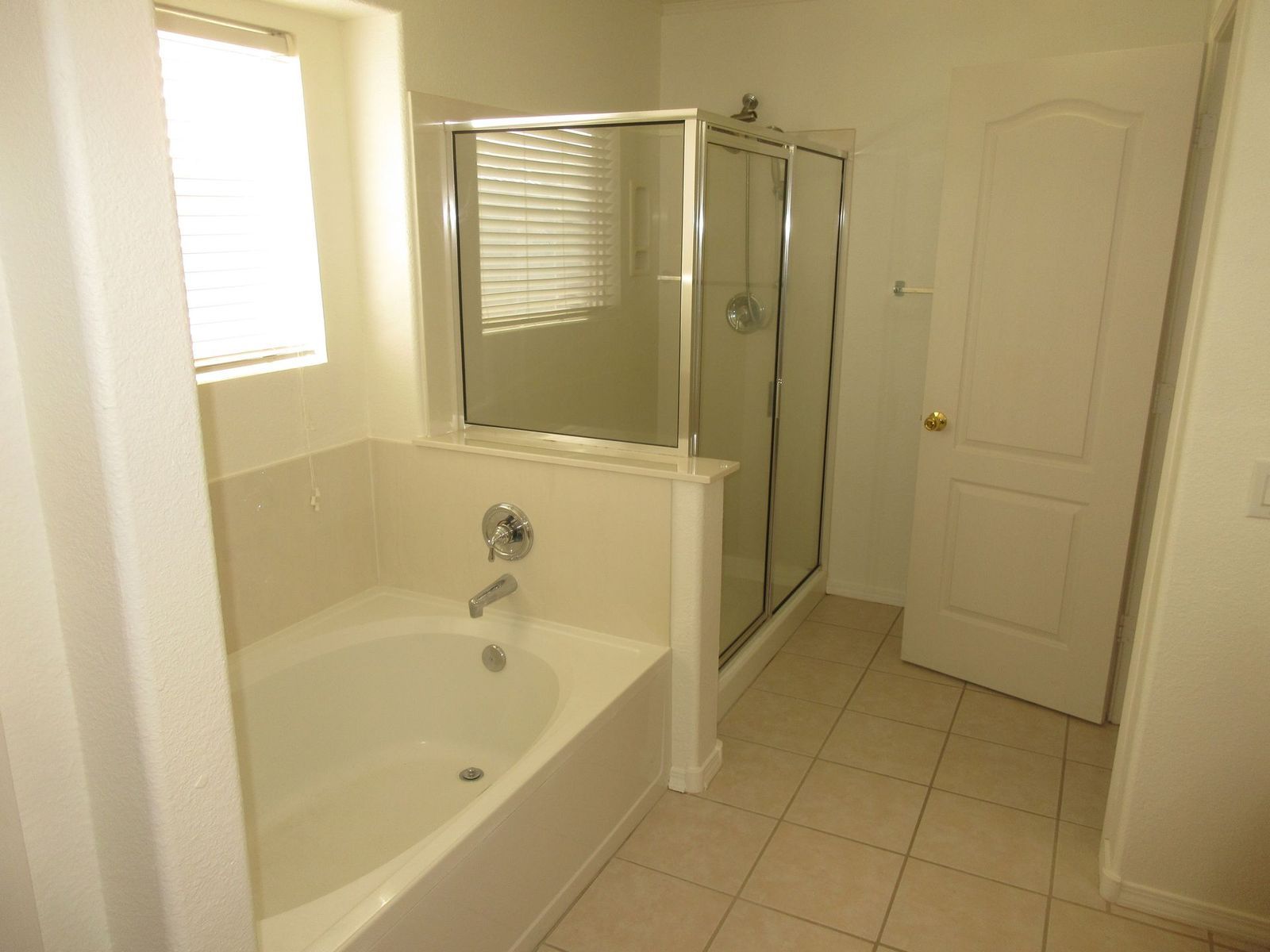 Bathroom with bathtub, shower, window with blinds, and closed door.