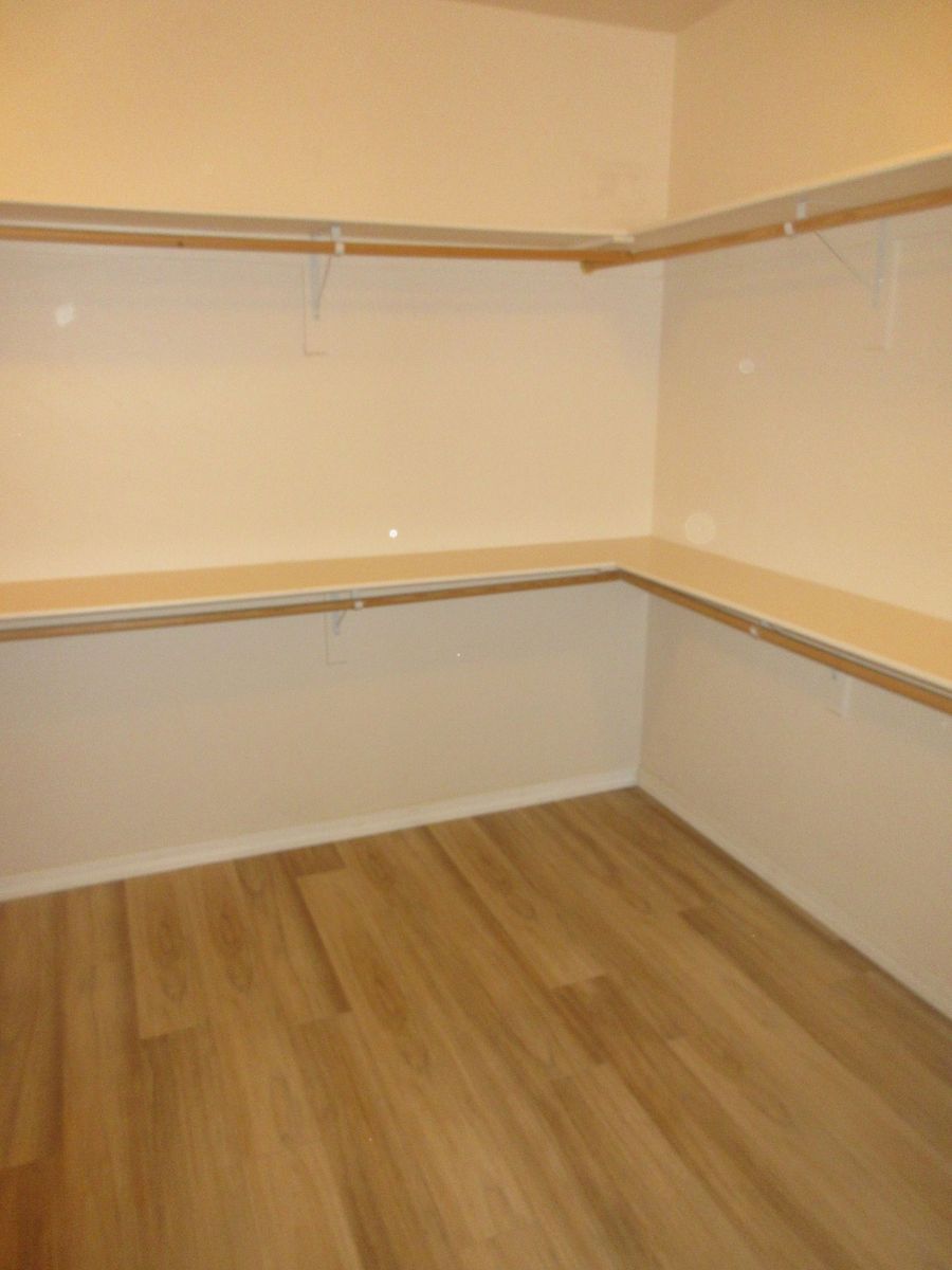 Empty walk-in closet with tan wooden floor, white walls, and built-in shelves and rods.