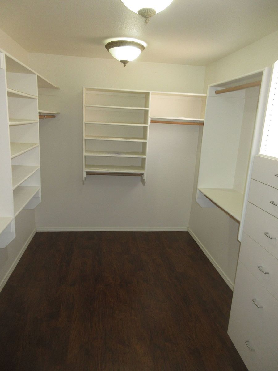 Empty walk-in closet with white shelving and dark wood floor.
