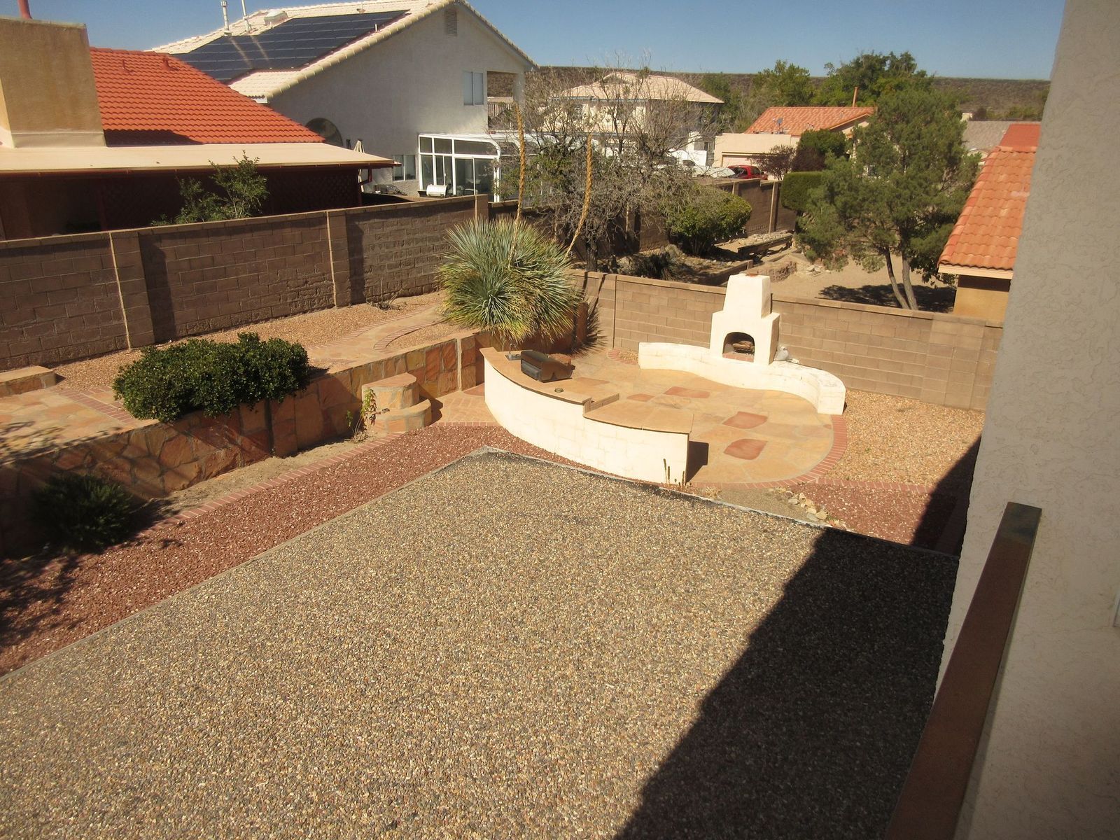 Backyard patio with gravel, a brick oven, and surrounding houses.