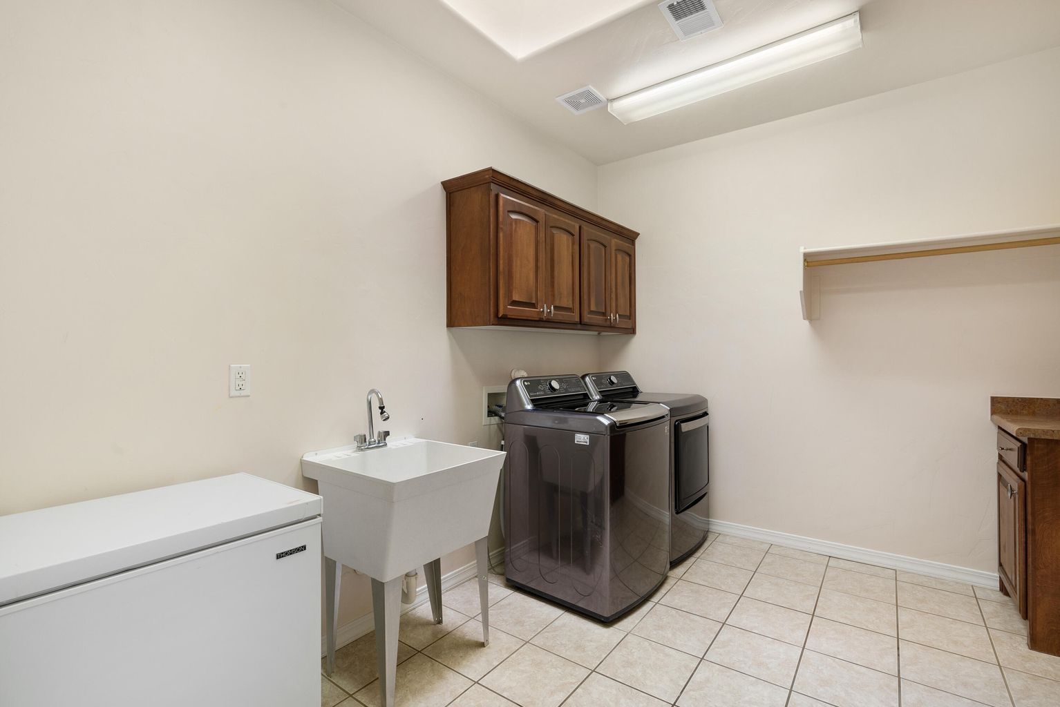 Laundry room with a washing machine, dryer, sink, cabinet, and freezer.