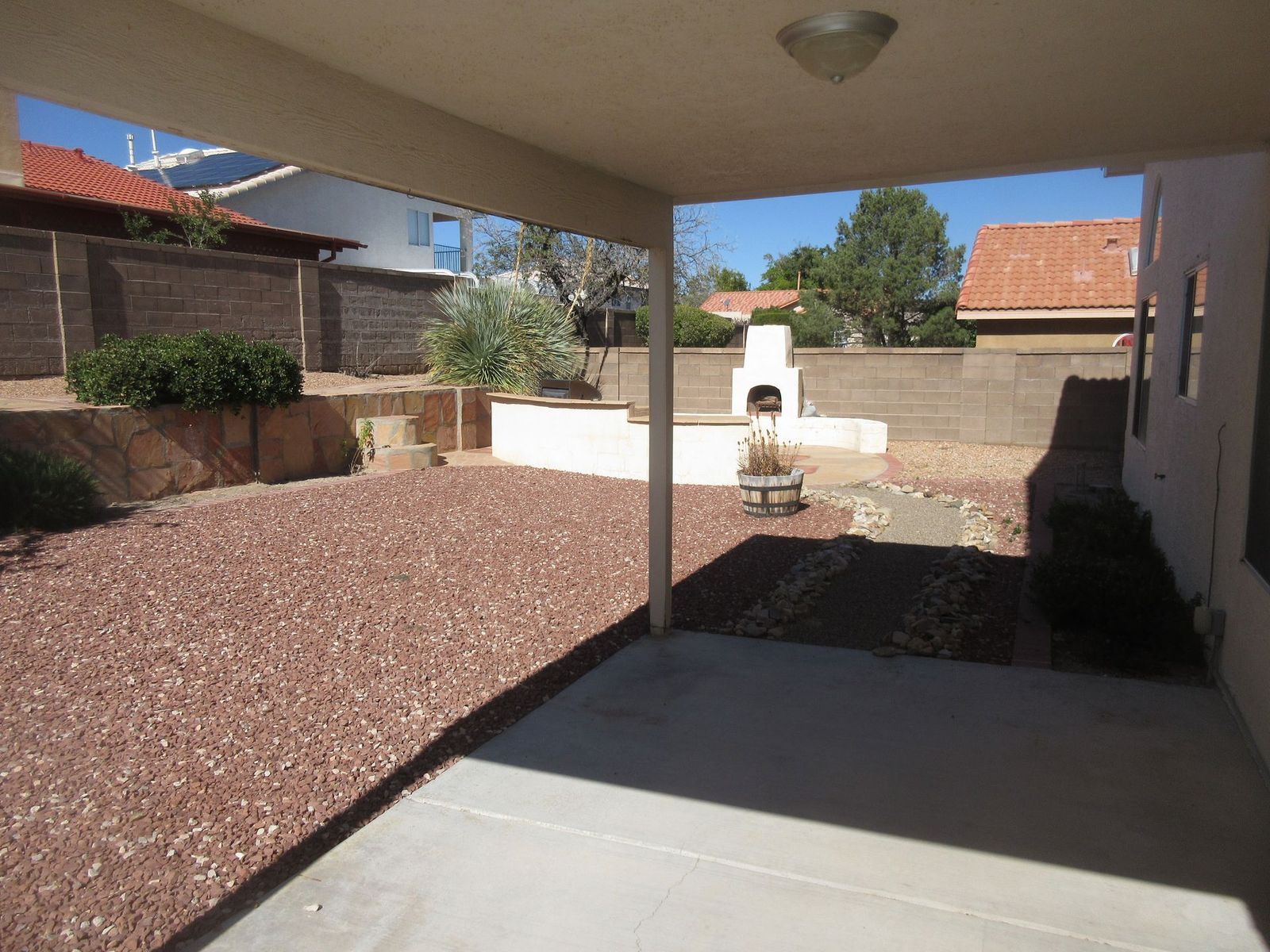 Covered patio overlooking a backyard with red gravel, a fireplace, and a low wall.