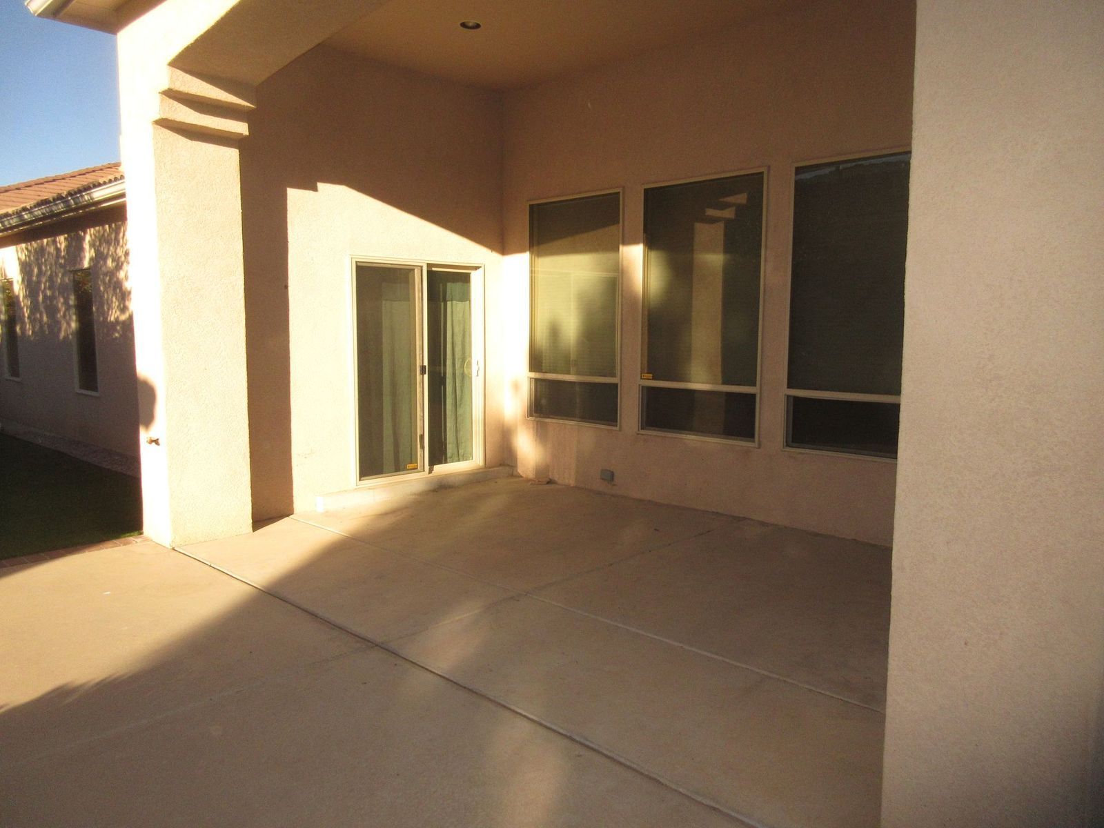 Covered patio with concrete floor and large windows reflecting sunlight.