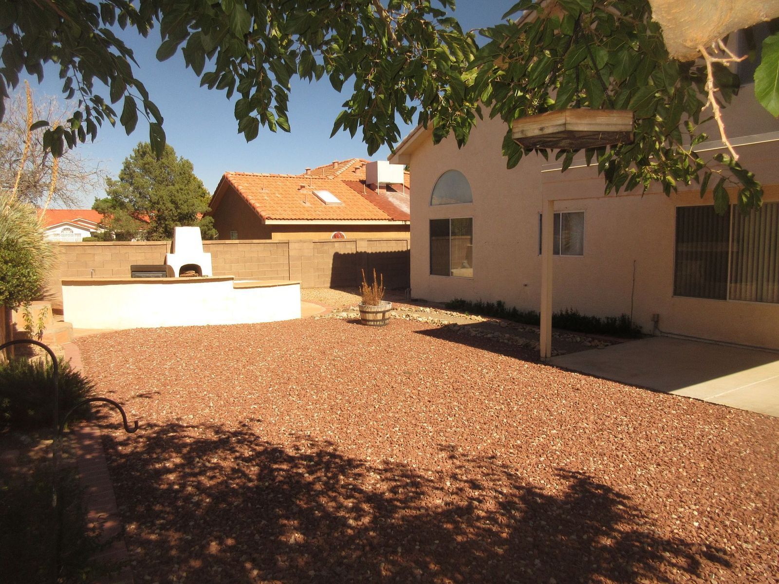 Backyard with stone ground, white stucco house, brown fence, and trees overhead.