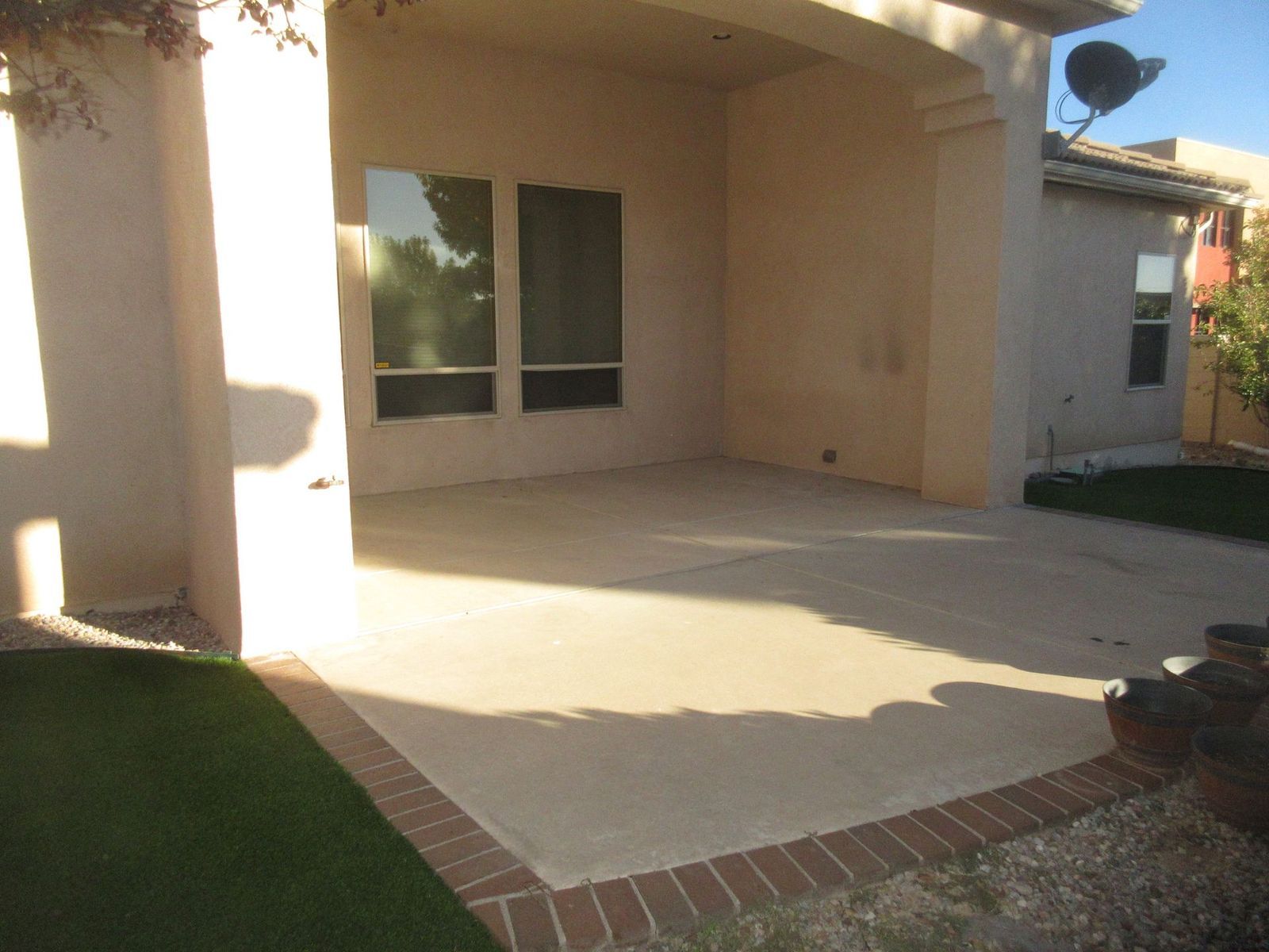 Concrete patio with brick border, attached to a light-colored stucco building; green grass surrounds.