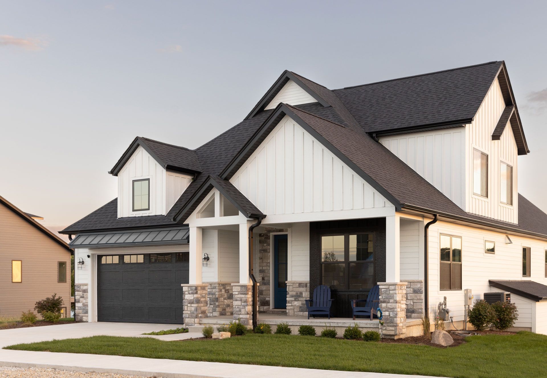 White farmhouse with black roof, garage door, and stone accents.