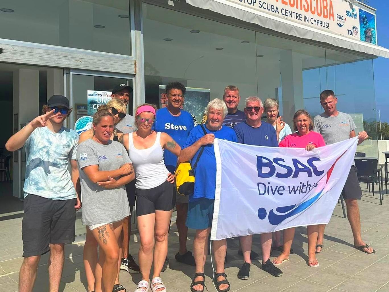 A group of people standing in front of a building holding a bsac flag.
