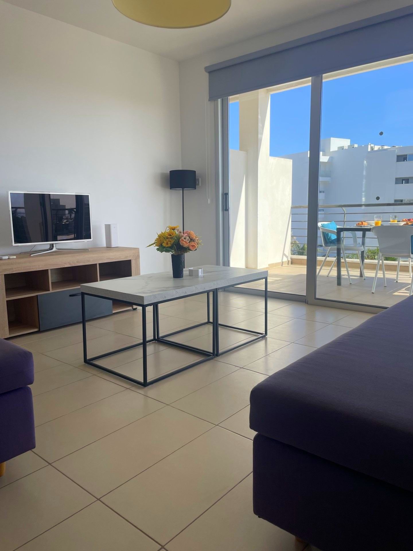 A living room with two coffee tables , a couch , a television and a balcony.