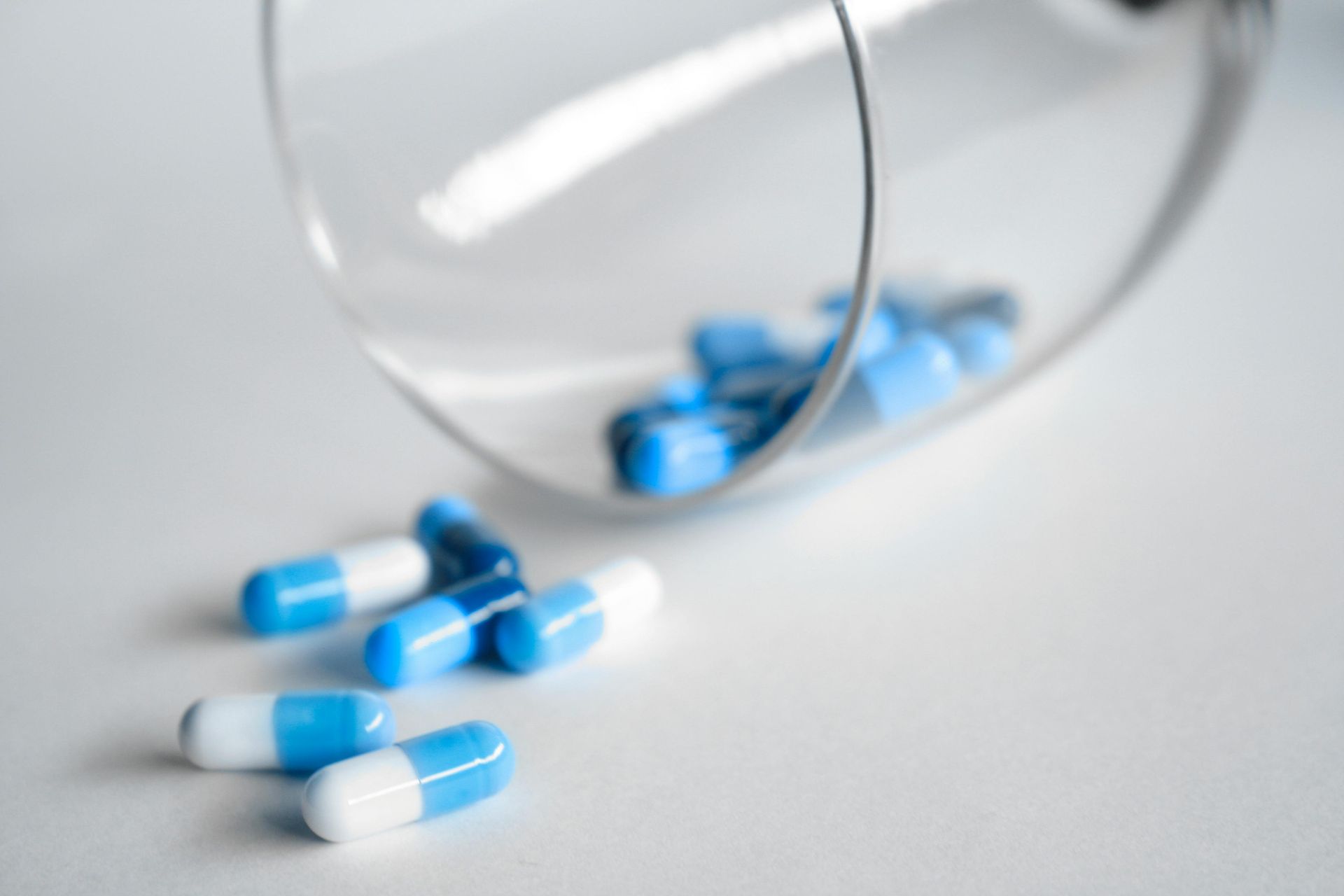 Blue and white pills are pouring out of a glass on a table.
