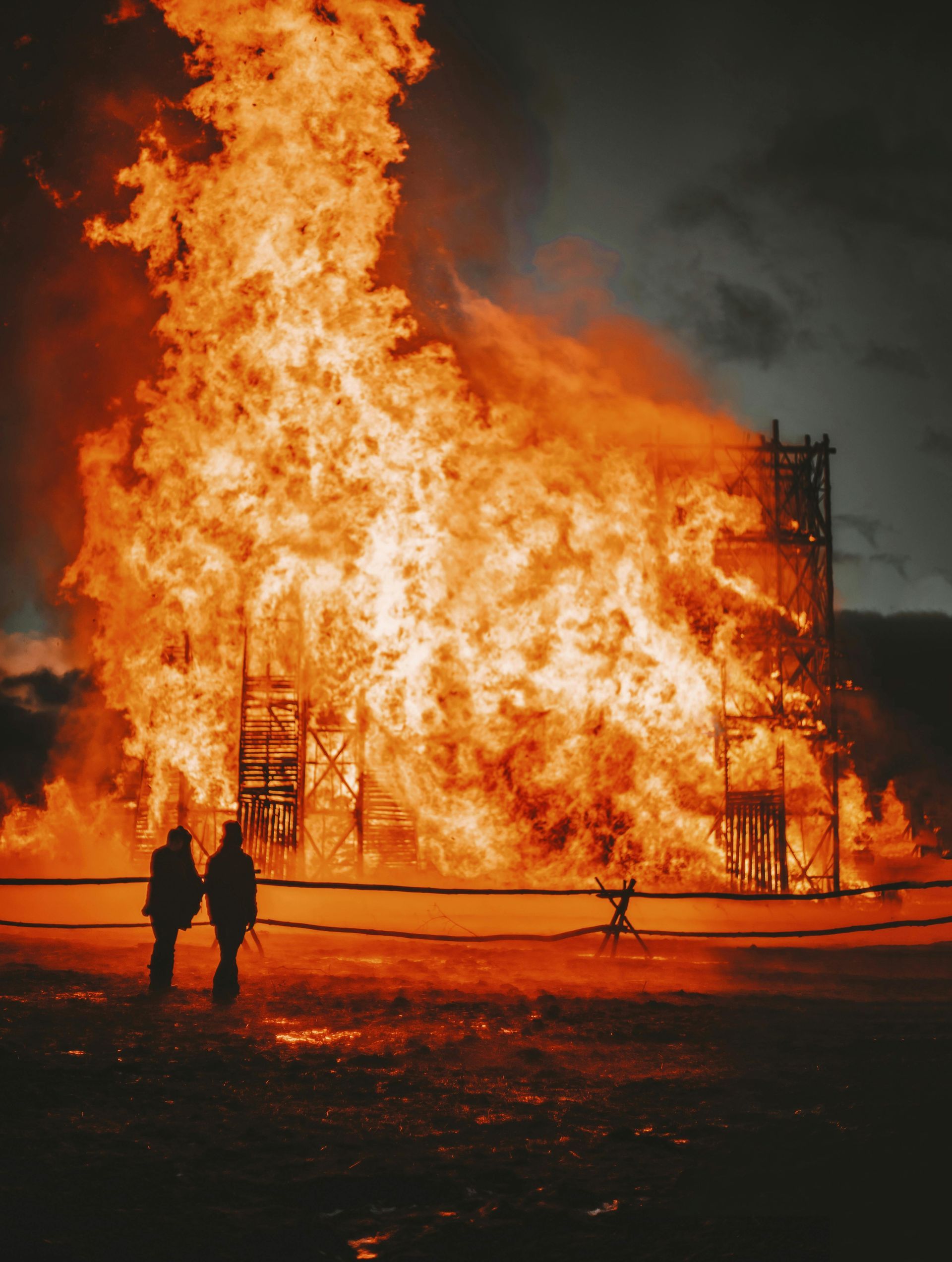 Two firefighters are standing in front of a large fire.