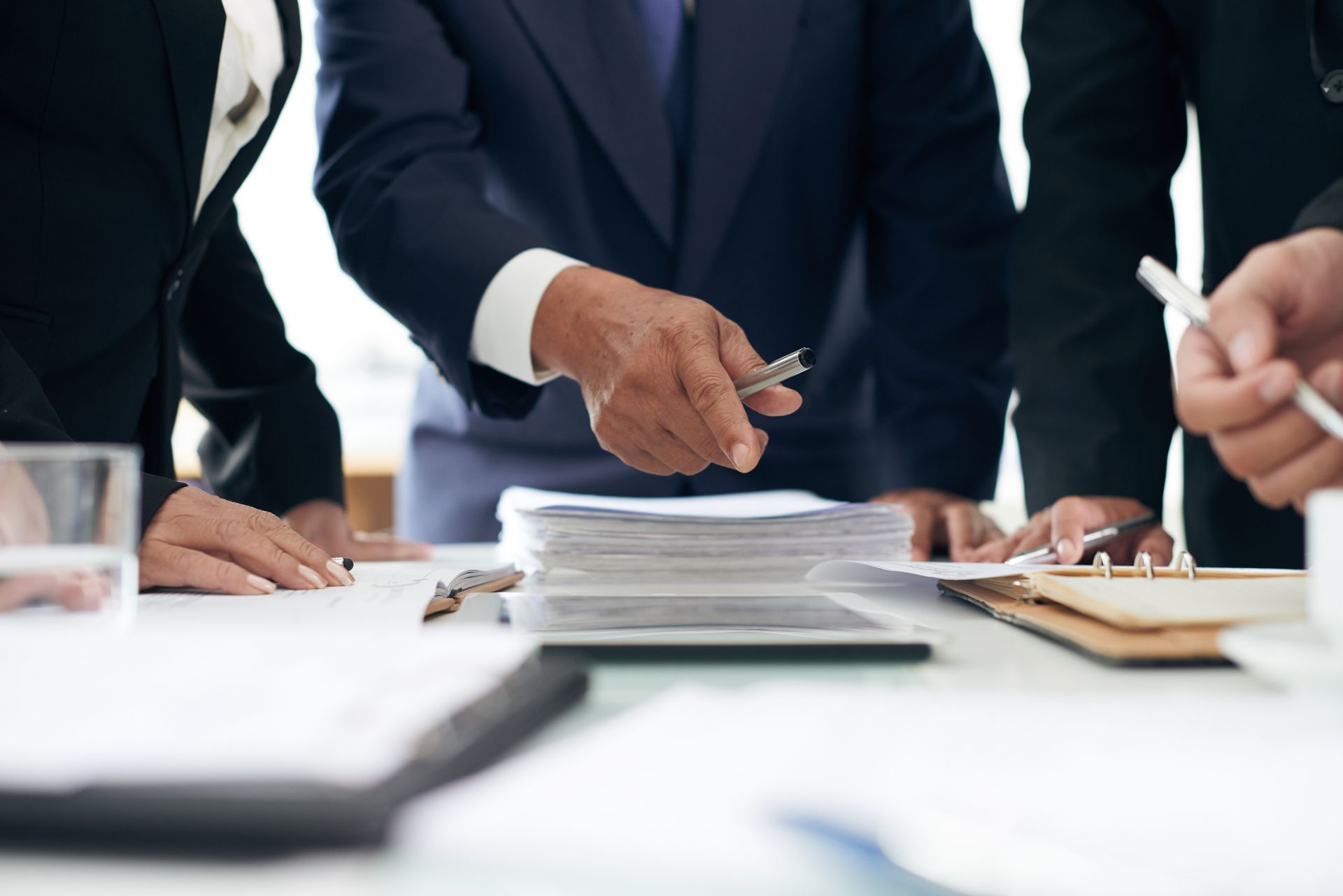 People in business suits reviewing documents on a table, one pointing at papers.