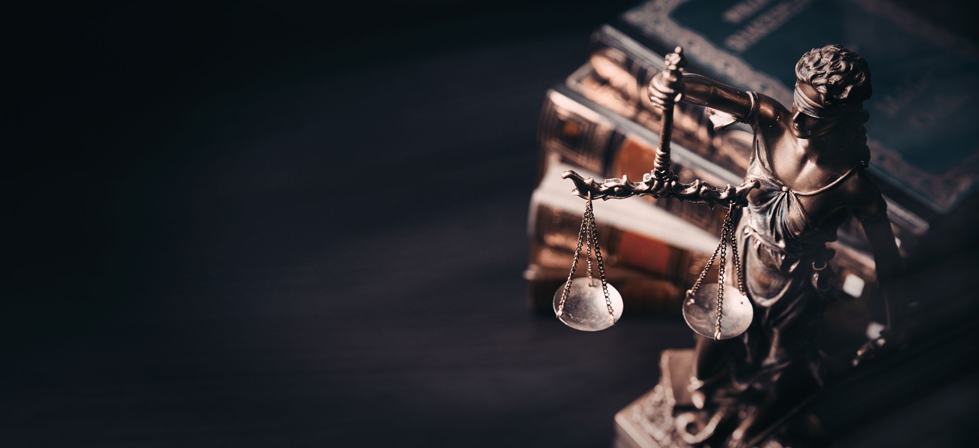 Statue of Lady Justice with scales, next to a stack of books. Dark, moody setting.